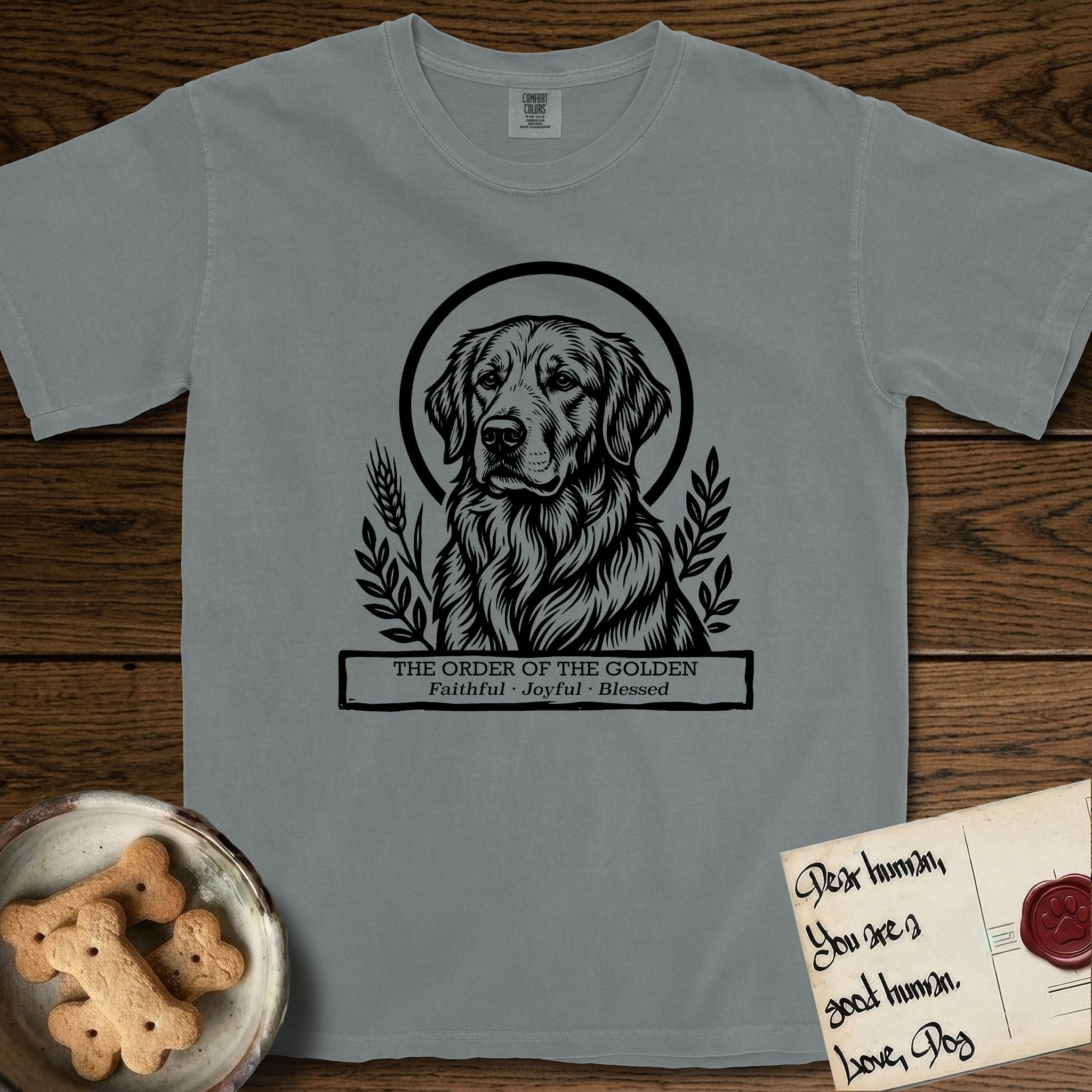 Holy Orders Golden Retriever T-Shirt flat lay in Granite, featuring a bold black-and-white linocut saint-medallion portrait of a Golden Retriever.