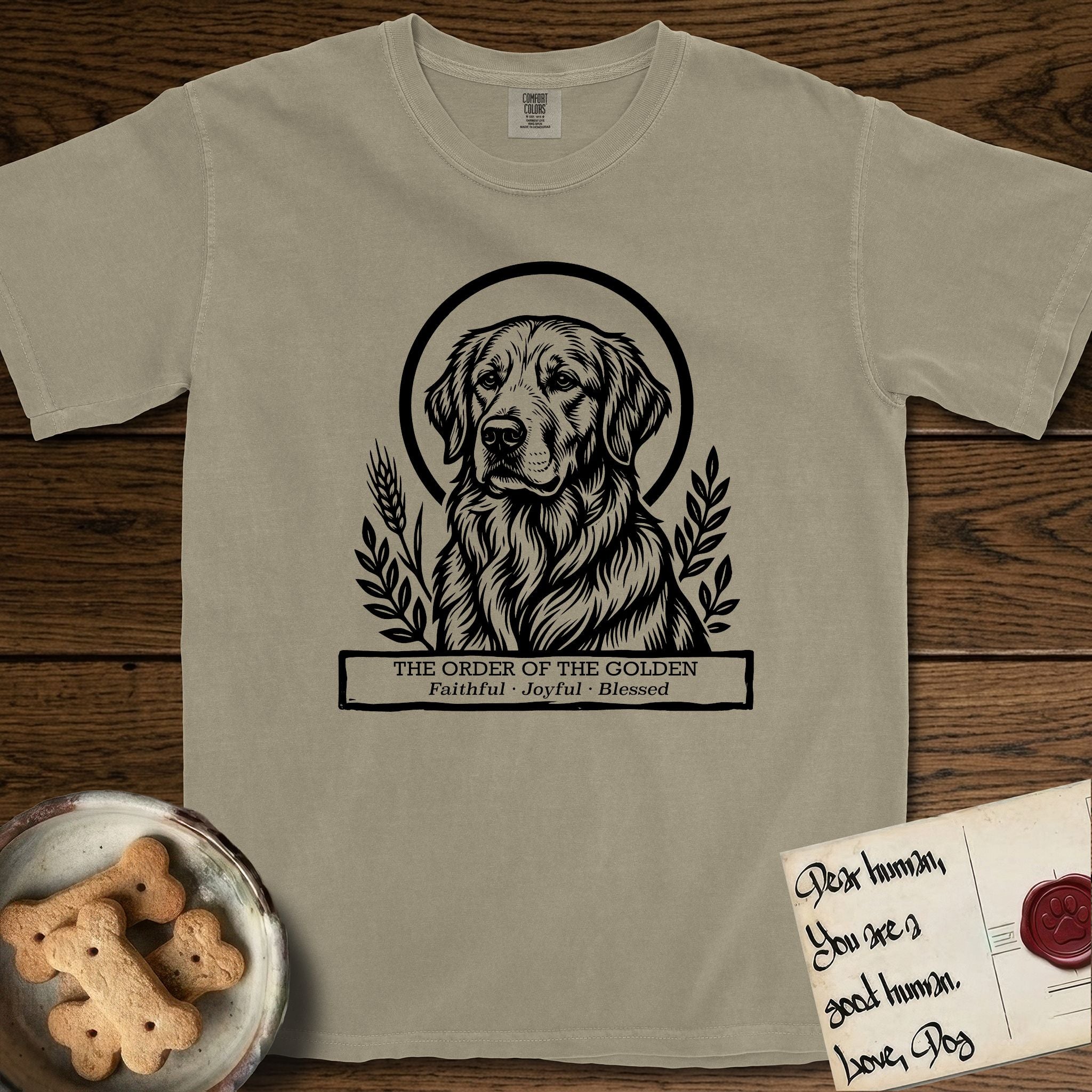 Holy Orders Golden Retriever T-Shirt flat lay in Khaki, featuring a bold black-and-white linocut saint-medallion portrait of a Golden Retriever.
