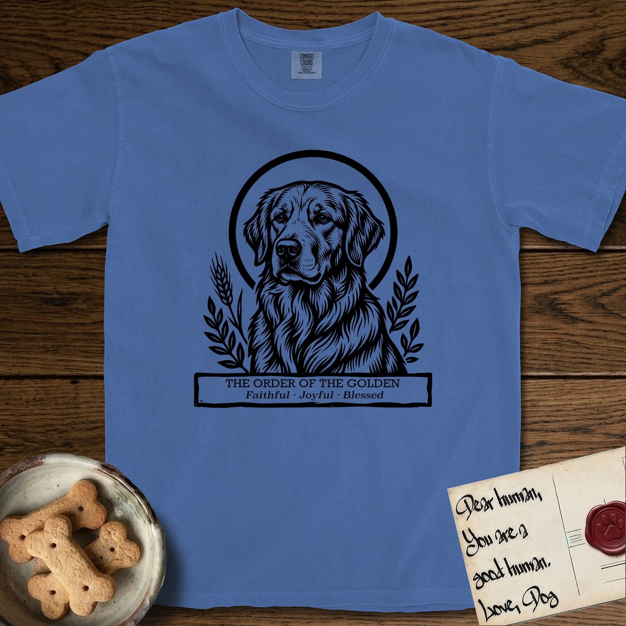 Holy Orders Golden Retriever T-Shirt flat lay in Mystic Blue, featuring a bold black-and-white linocut saint-medallion portrait of a Golden Retriever.