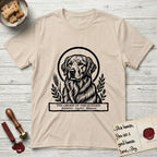 Holy Orders Golden Retriever T-Shirt flat lay in Sand, featuring a bold black-and-white linocut saint-medallion portrait of a Golden Retriever.