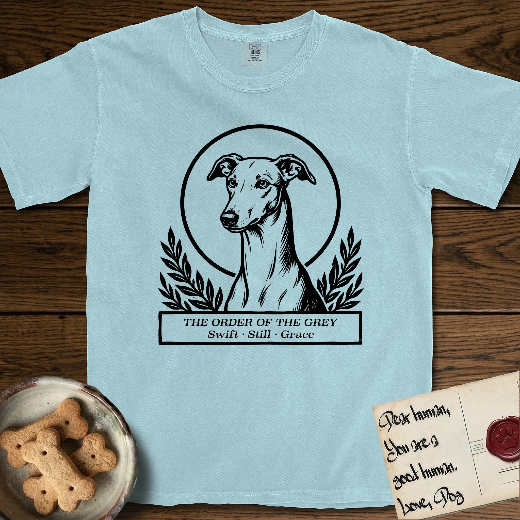 Holy Orders Greyhound T-Shirt flat lay in Chambray, featuring a bold black-and-white linocut saint-medallion portrait of a Greyhound.