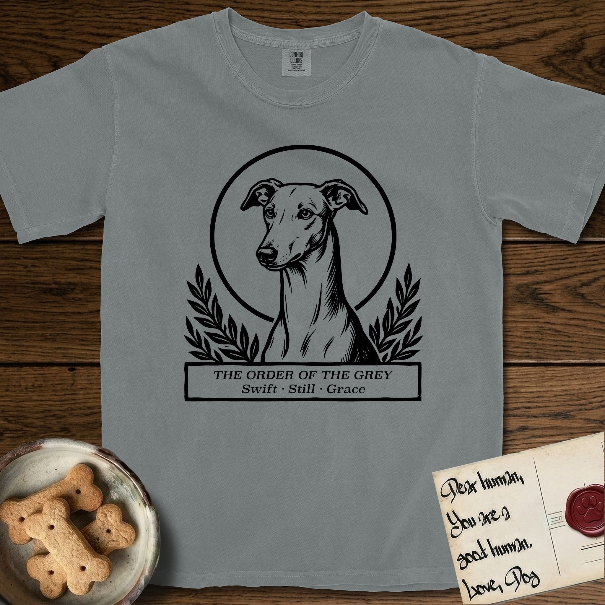 Holy Orders Greyhound T-Shirt flat lay in Granite, featuring a bold black-and-white linocut saint-medallion portrait of a Greyhound.