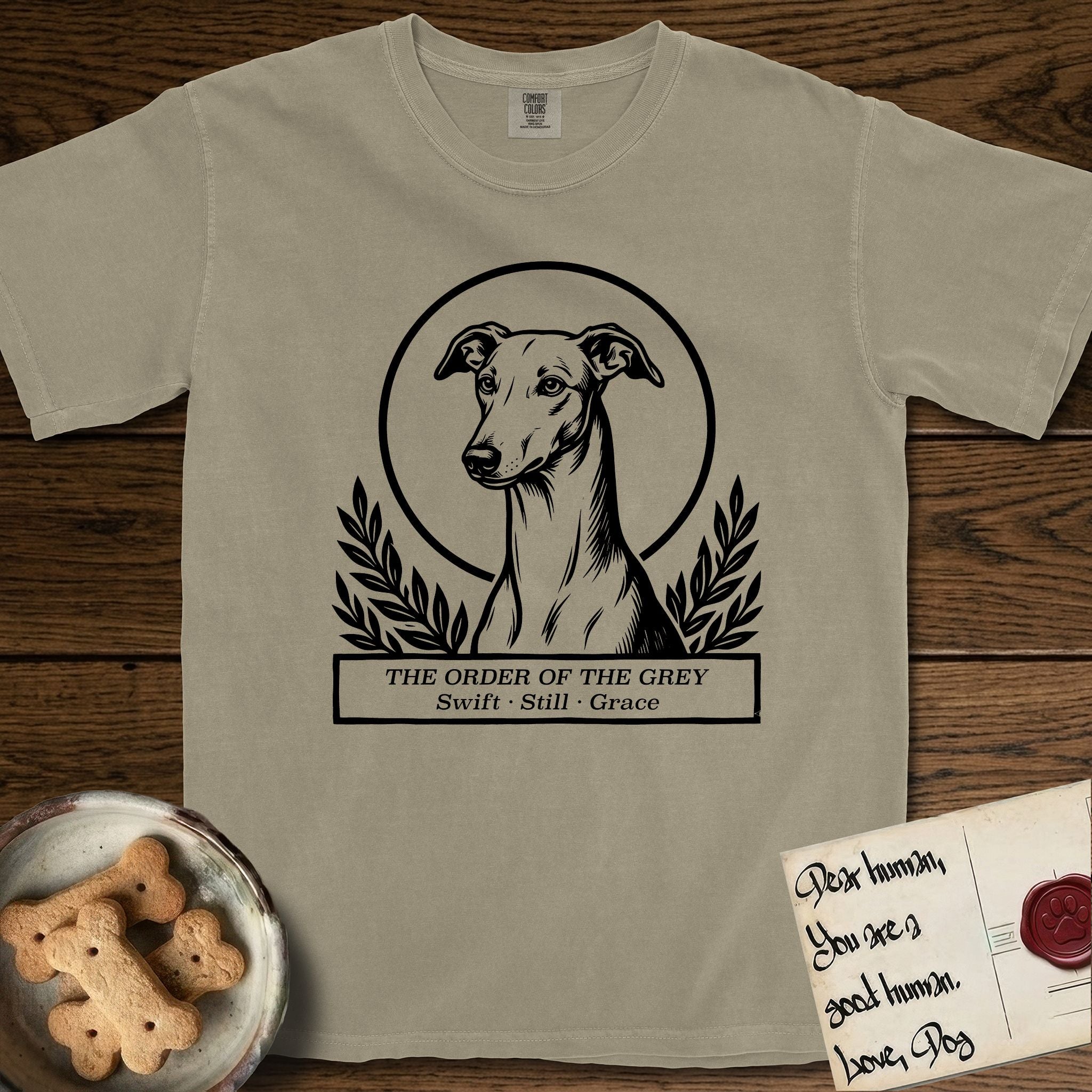 Holy Orders Greyhound T-Shirt flat lay in Khaki, featuring a bold black-and-white linocut saint-medallion portrait of a Greyhound.