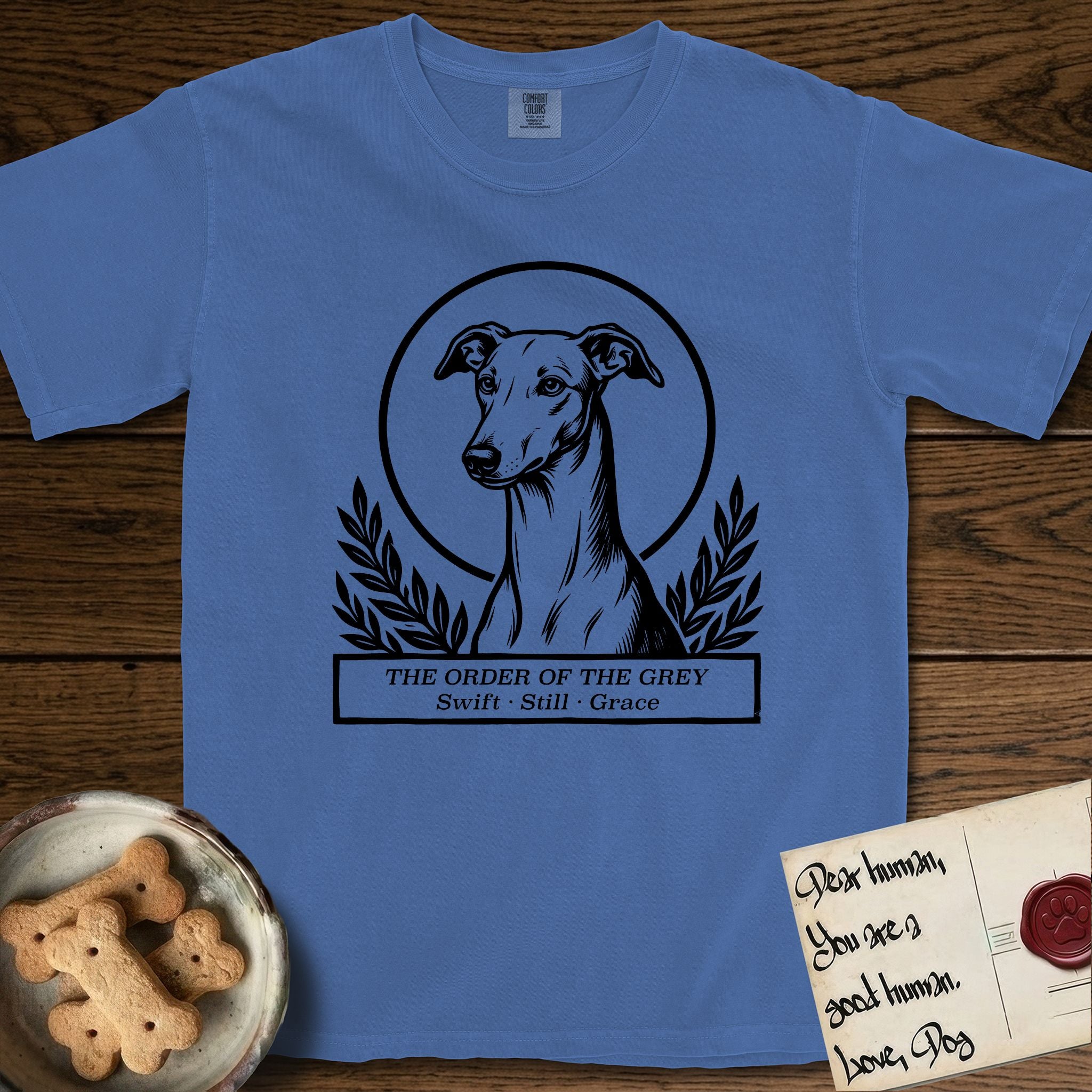 Holy Orders Greyhound T-Shirt flat lay in Mystic Blue, featuring a bold black-and-white linocut saint-medallion portrait of a Greyhound.