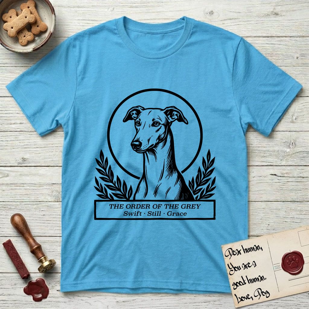 Holy Orders Greyhound T-Shirt flat lay in Sky, featuring a bold black-and-white linocut saint-medallion portrait of a Greyhound.