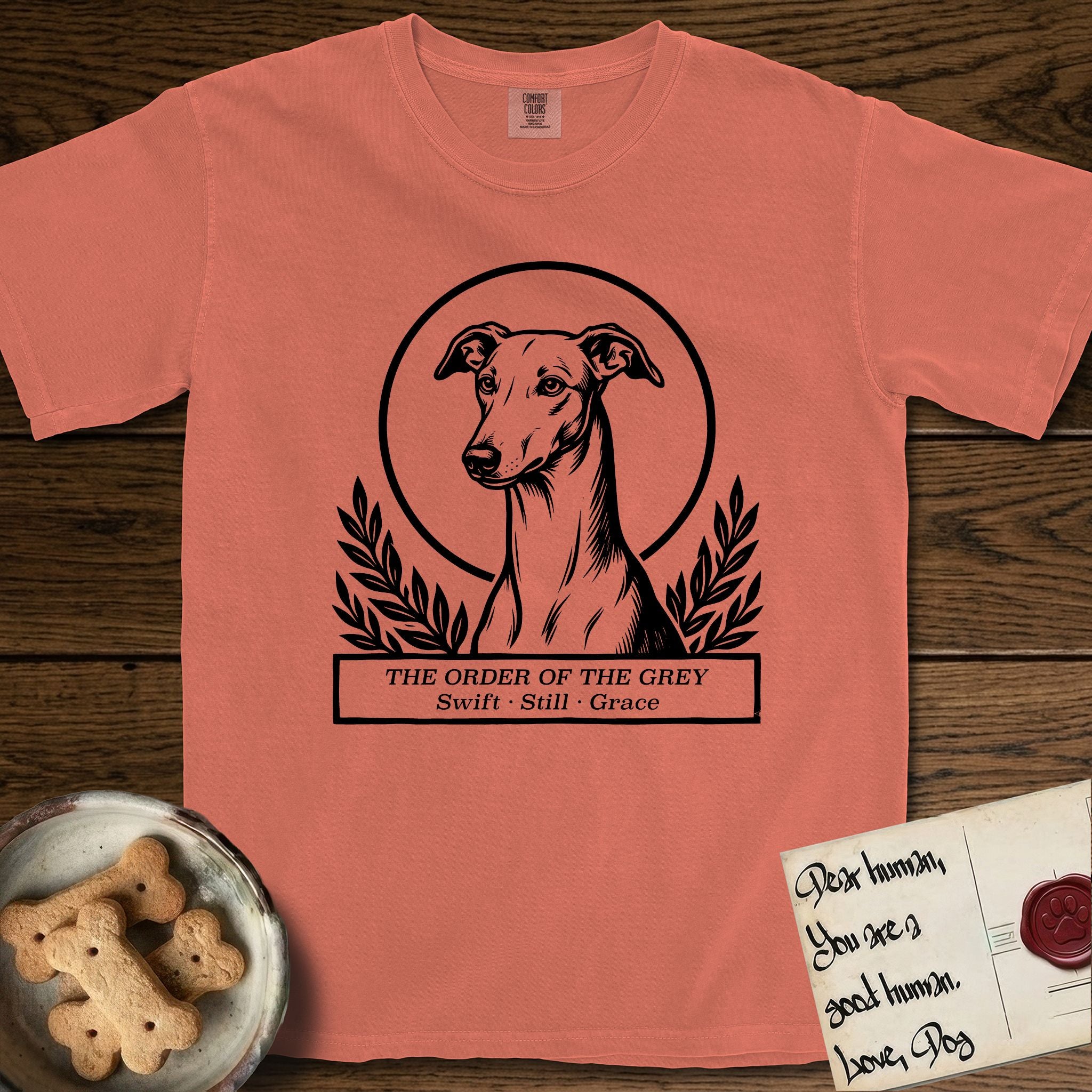 Holy Orders Greyhound T-Shirt flat lay in Terracotta, featuring a bold black-and-white linocut saint-medallion portrait of a Greyhound.