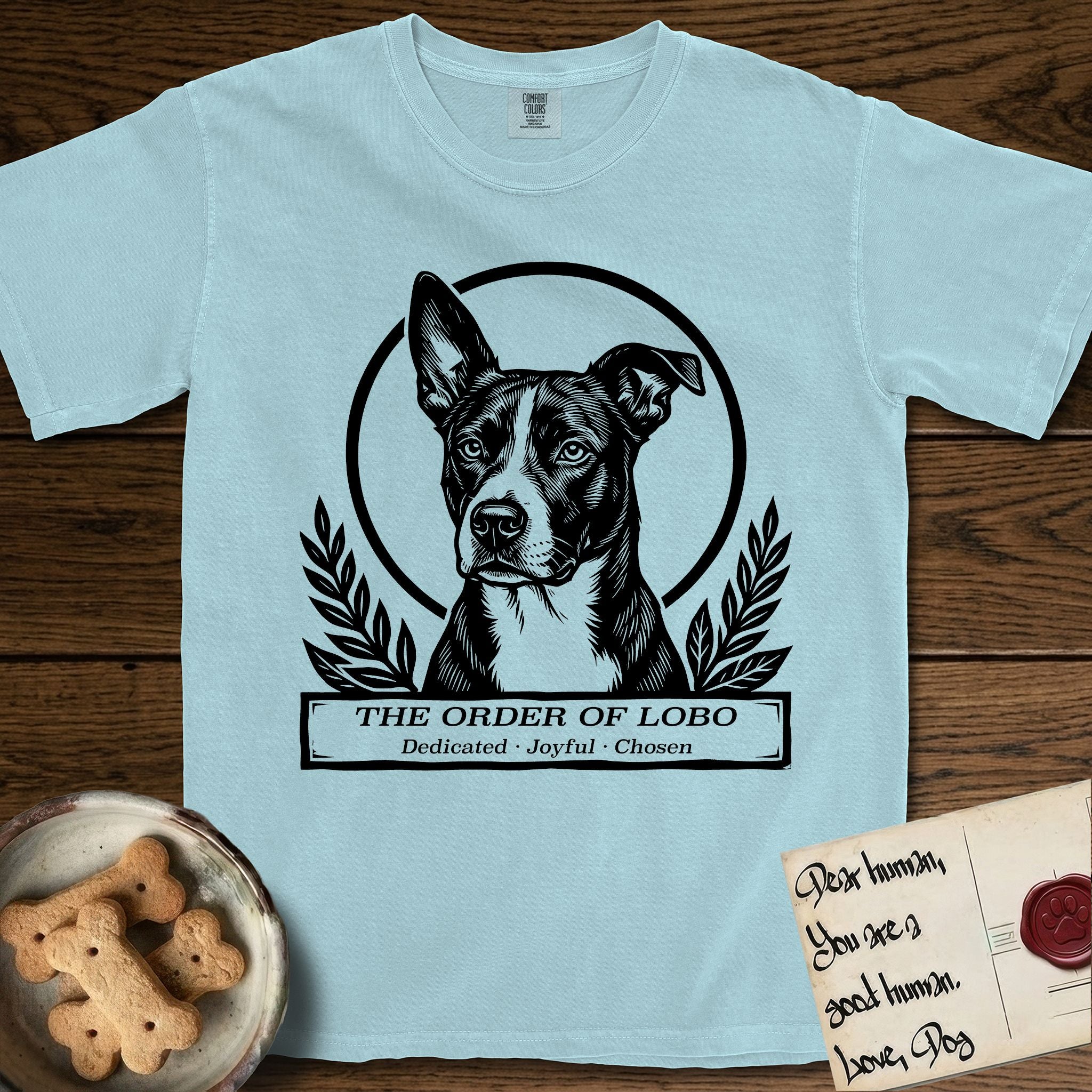 Holy Orders Lobo T-Shirt flat lay in Chambray, featuring a bold black-and-white linocut saint-medallion portrait of Lobo, an Australian Cattle Dog and Pitbull mix with a white facial blaze.