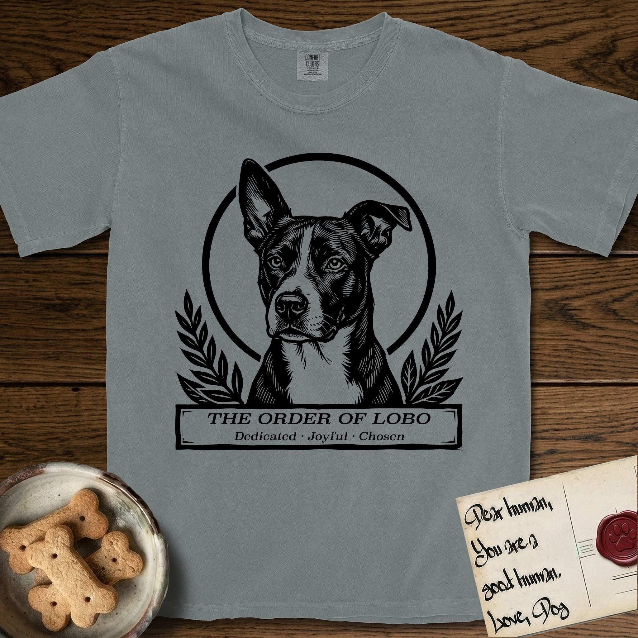 Holy Orders Lobo T-Shirt flat lay in Granite, featuring a bold black-and-white linocut saint-medallion portrait of Lobo, an Australian Cattle Dog and Pitbull mix with a white facial blaze.