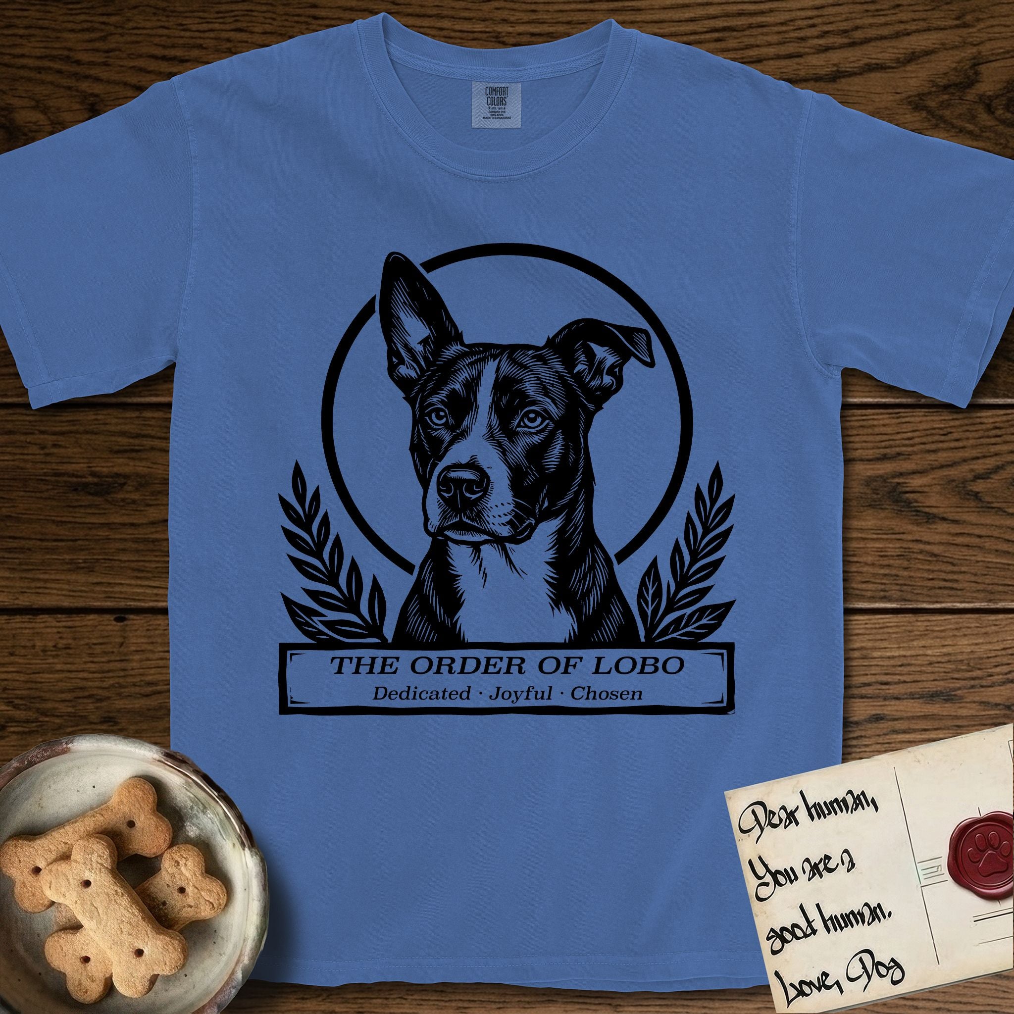 Holy Orders Lobo T-Shirt flat lay in Mystic Blue, featuring a bold black-and-white linocut saint-medallion portrait of Lobo, an Australian Cattle Dog and Pitbull mix with a white facial blaze.