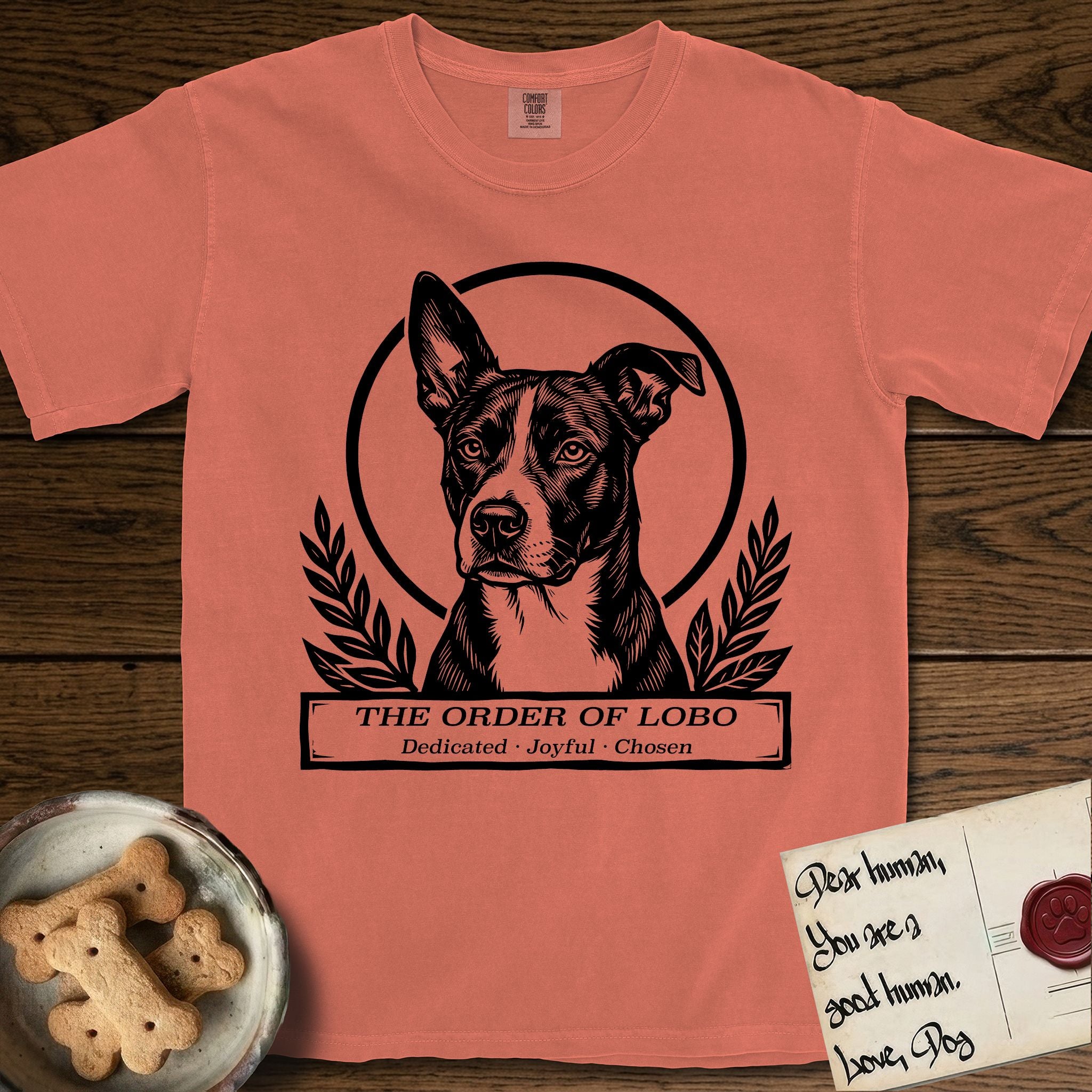 Holy Orders Lobo T-Shirt flat lay in Terracotta, featuring a bold black-and-white linocut saint-medallion portrait of Lobo, an Australian Cattle Dog and Pitbull mix with a white facial blaze.