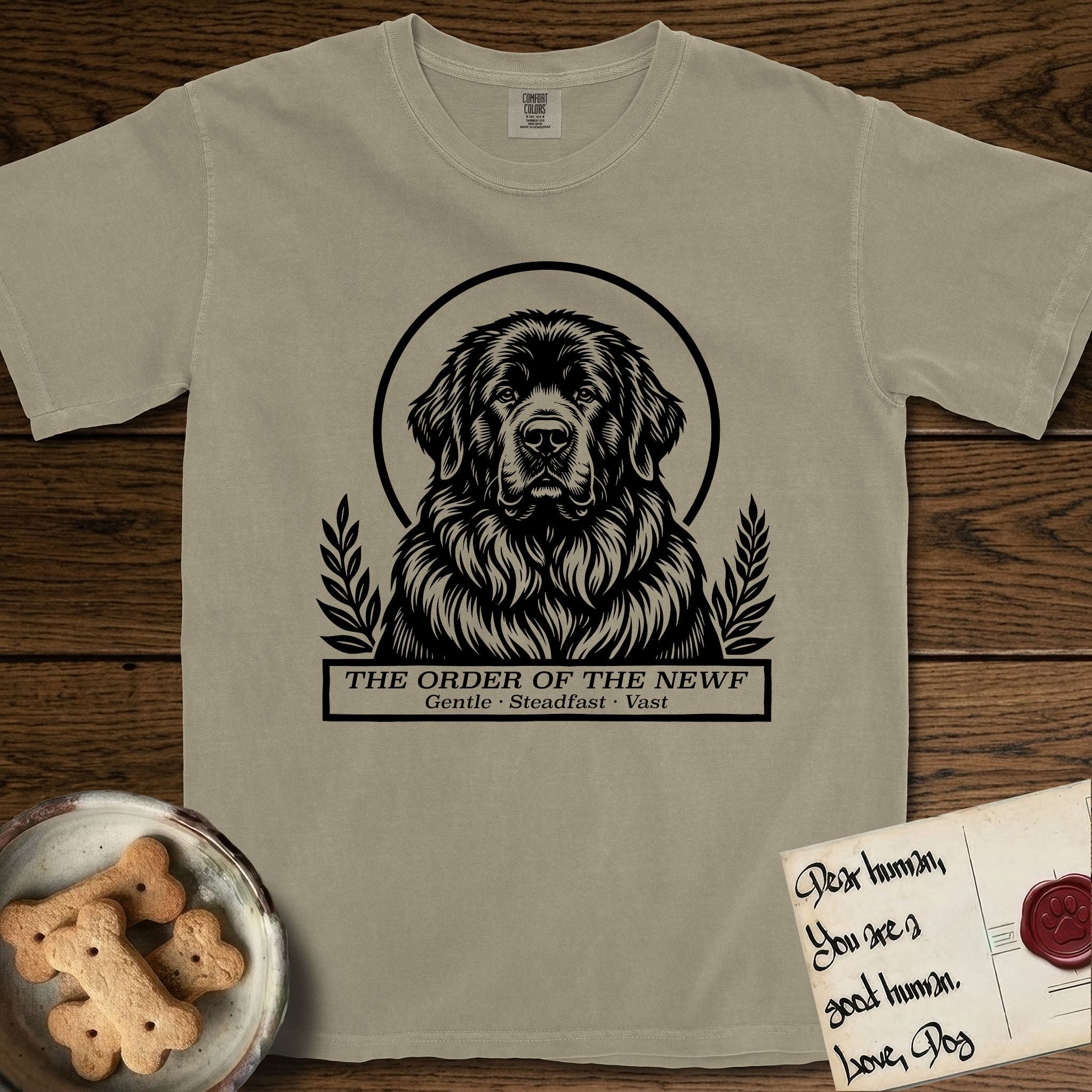 Holy Orders Newfoundland T-Shirt flat lay in Khaki, featuring a bold black-and-white linocut saint-medallion portrait of a Newfoundland.