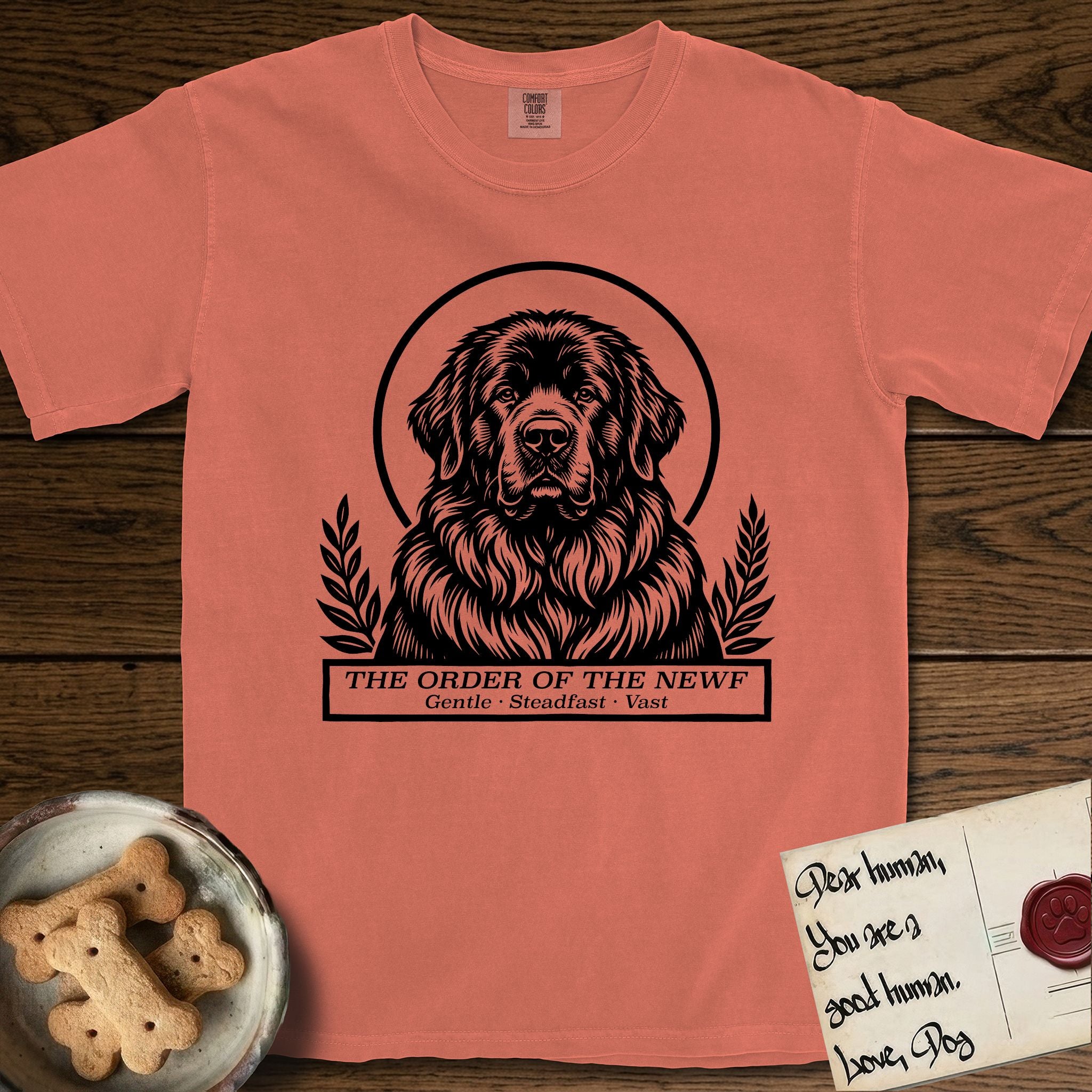 Holy Orders Newfoundland T-Shirt flat lay in Terracotta, featuring a bold black-and-white linocut saint-medallion portrait of a Newfoundland.