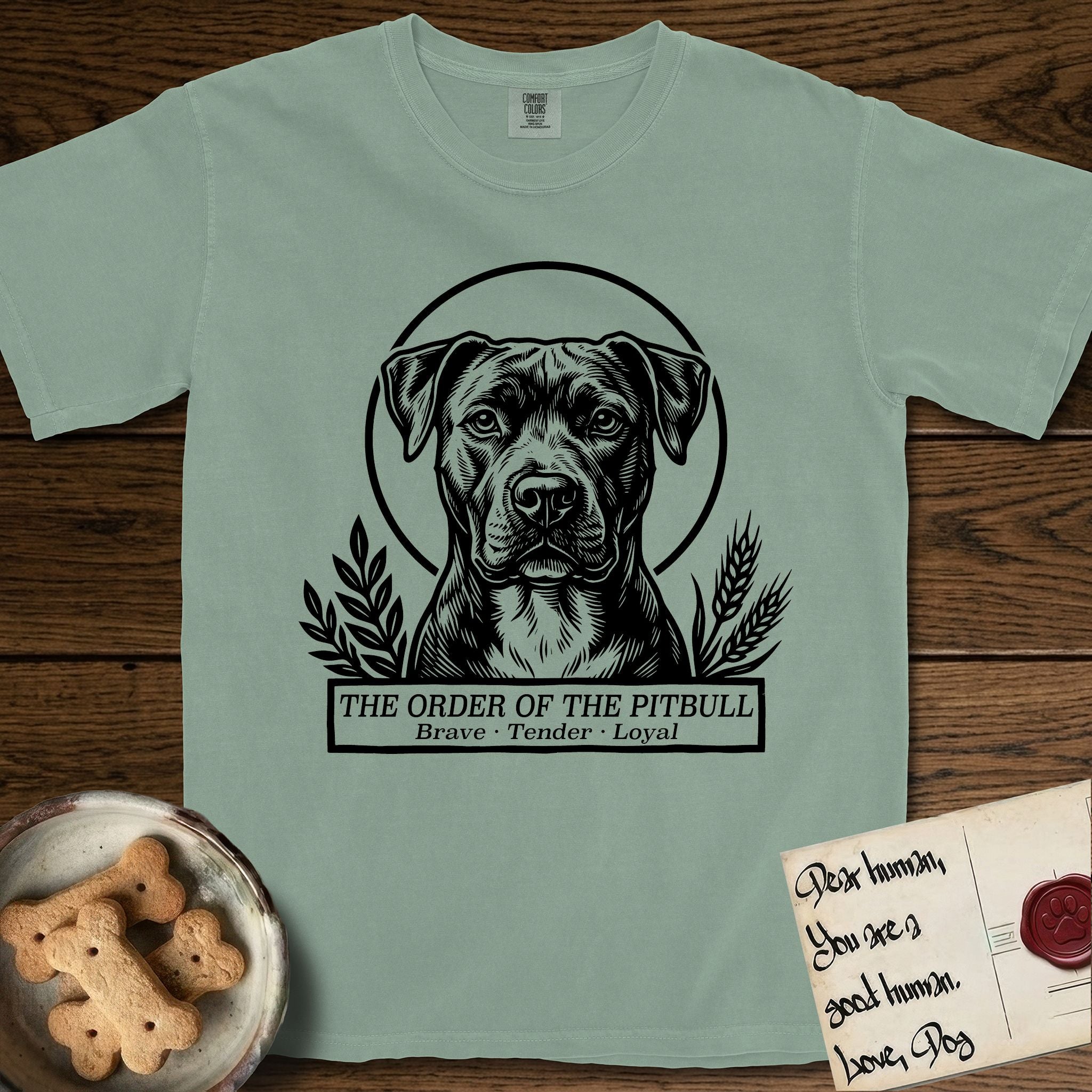 Holy Orders Pitbull T-Shirt flat lay in Bay, featuring a bold black-and-white linocut saint-medallion portrait of a Pitbull.