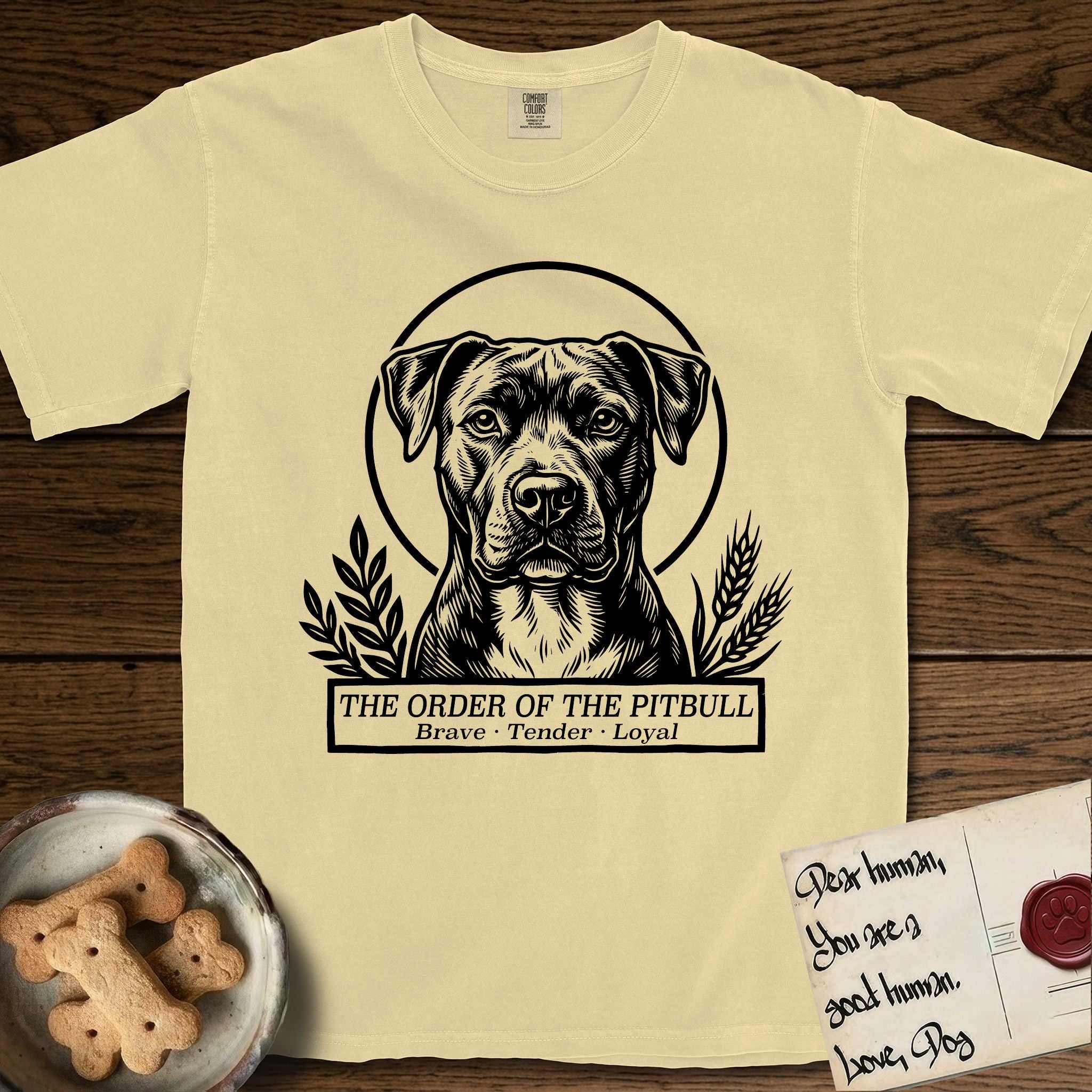 Holy Orders Pitbull T-Shirt flat lay in Butter, featuring a bold black-and-white linocut saint-medallion portrait of a Pitbull.
