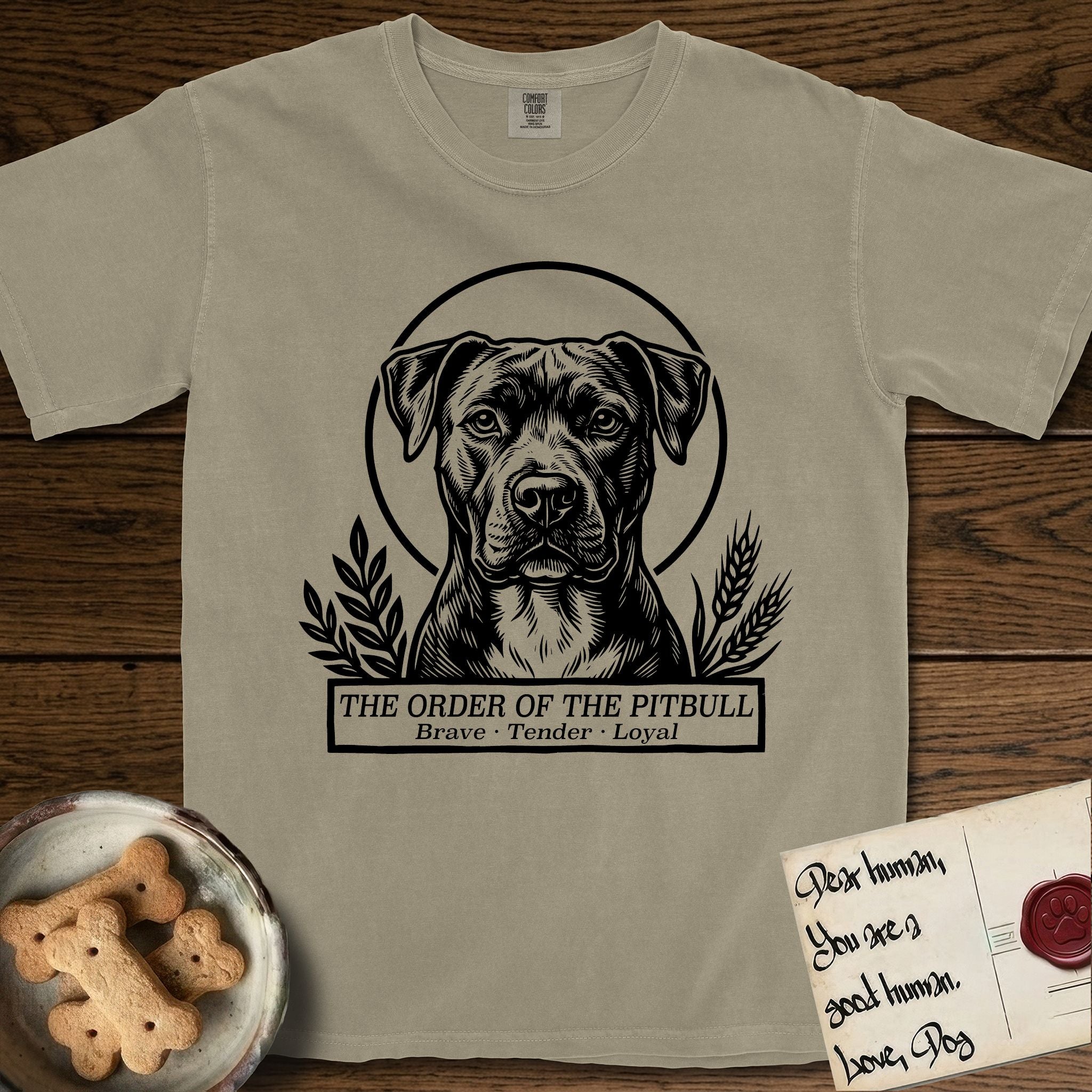Holy Orders Pitbull T-Shirt flat lay in Khaki, featuring a bold black-and-white linocut saint-medallion portrait of a Pitbull.