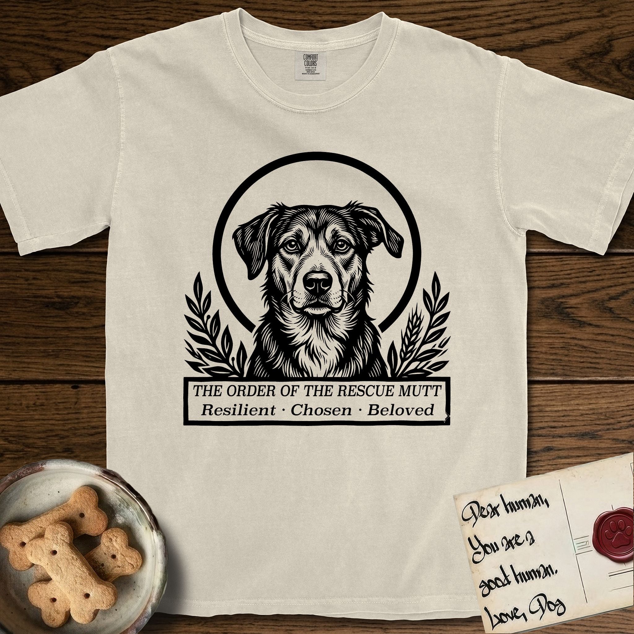Holy Orders Rescue Mutt T-Shirt flat lay in Ivory, featuring a bold black-and-white linocut saint-medallion portrait of a rescue mutt.