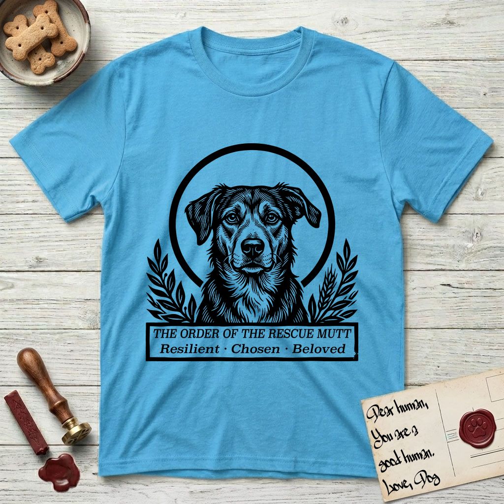 Holy Orders Rescue Mutt T-Shirt flat lay in Sky, featuring a bold black-and-white linocut saint-medallion portrait of a rescue mutt.