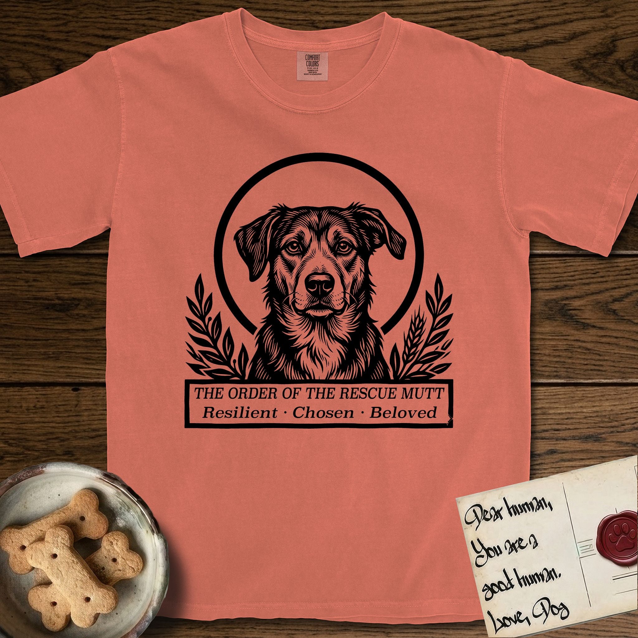 Holy Orders Rescue Mutt T-Shirt flat lay in Terracotta, featuring a bold black-and-white linocut saint-medallion portrait of a rescue mutt.
