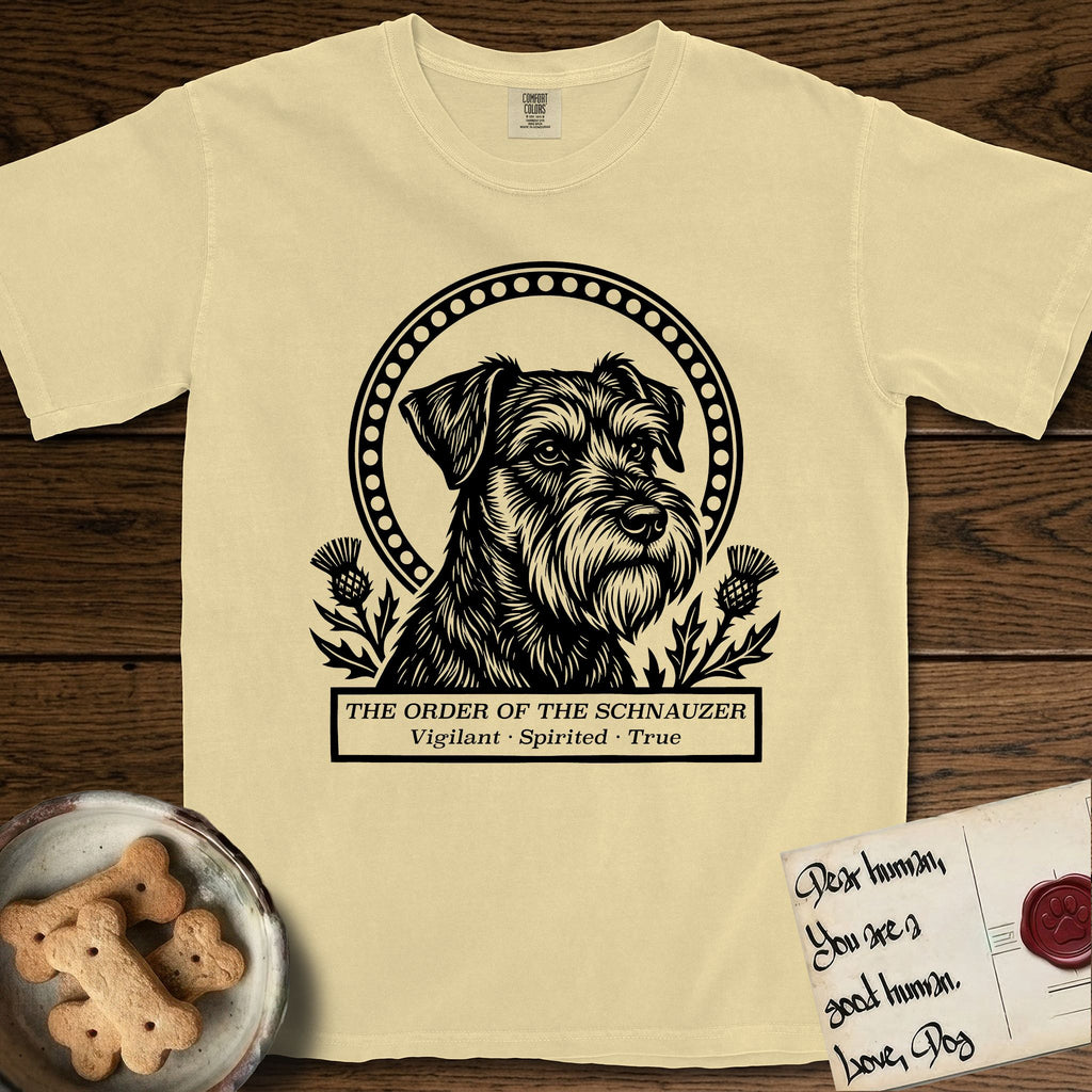 Holy Orders Schnauzer T-Shirt flat lay in Butter, featuring a bold black-and-white linocut saint-medallion portrait of a Schnauzer.