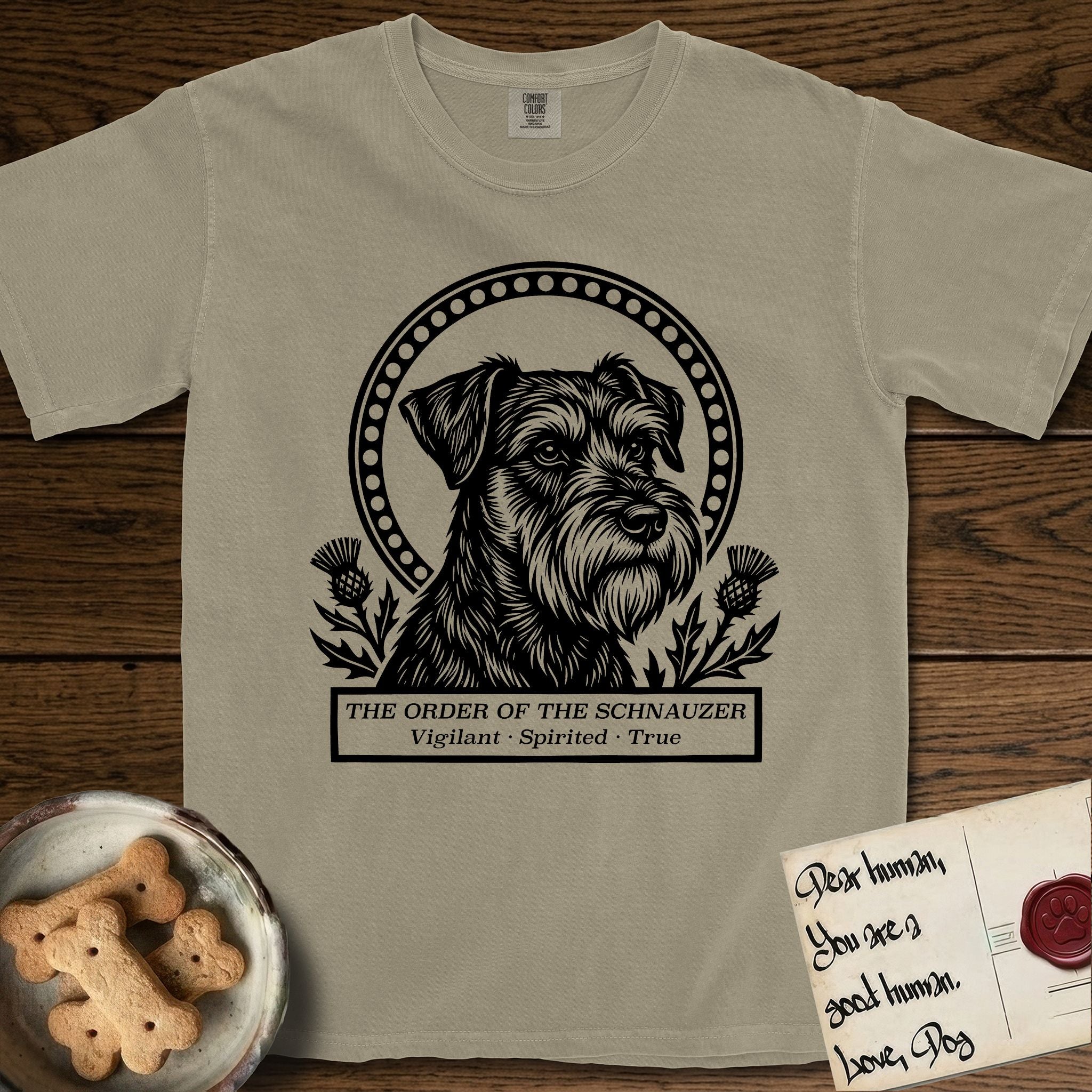 Holy Orders Schnauzer T-Shirt flat lay in Khaki, featuring a bold black-and-white linocut saint-medallion portrait of a Schnauzer.
