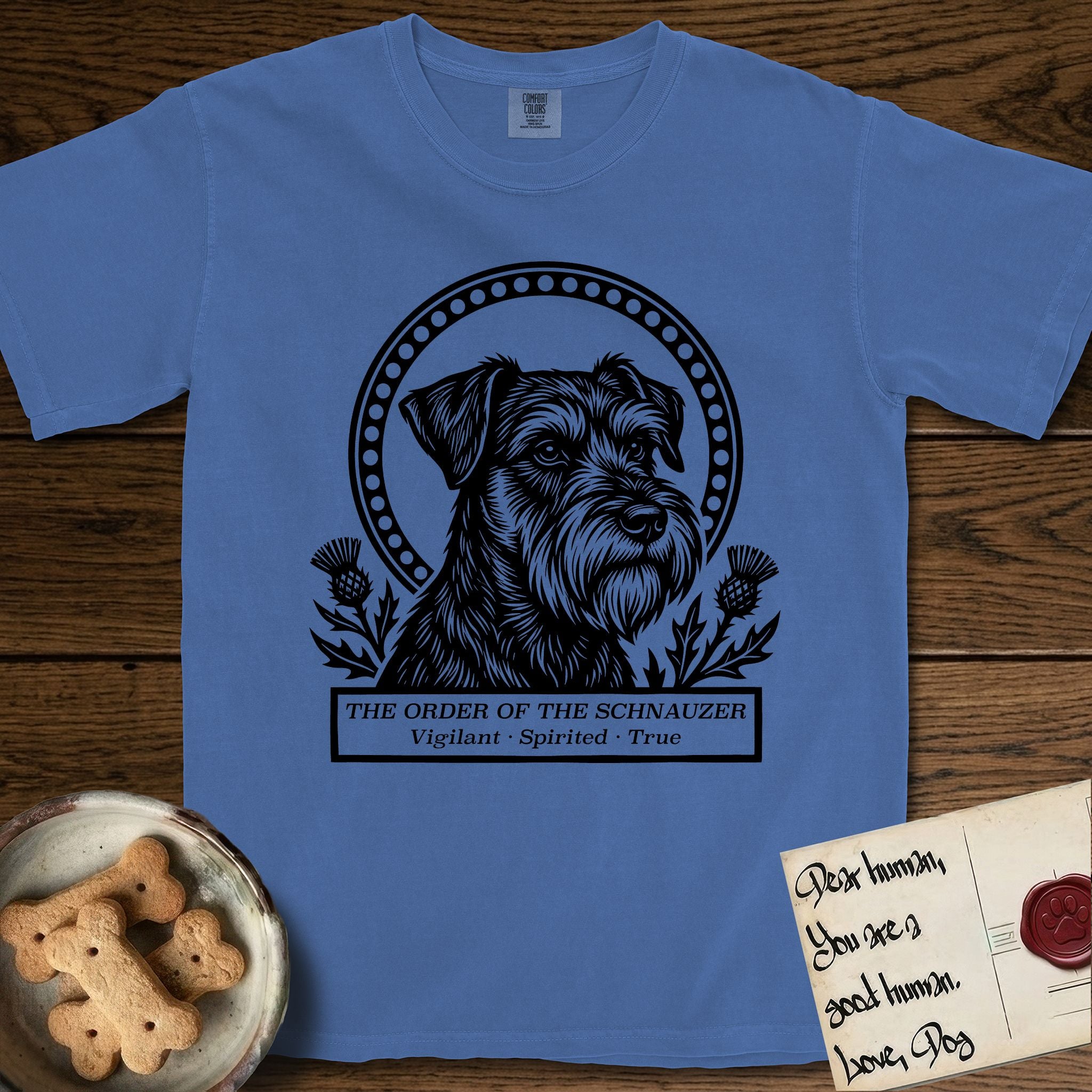 Holy Orders Schnauzer T-Shirt flat lay in Mystic Blue, featuring a bold black-and-white linocut saint-medallion portrait of a Schnauzer.