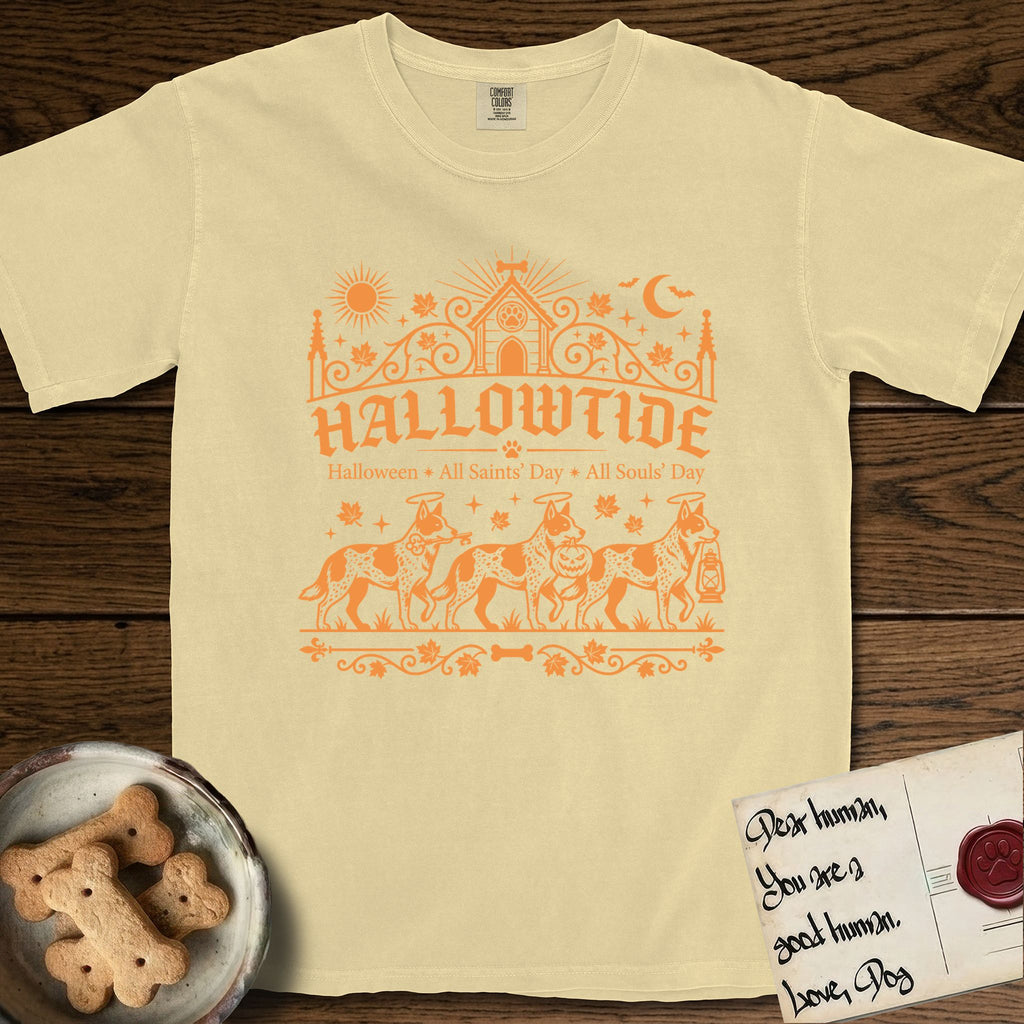 Hallowtide Australian Cattle Dog T-Shirt flat lay in Butter, featuring Orange one-color gothic illustration of three haloed speckled Australian Cattle Dogs walking in procession carrying a skeleton key, a scary jack-o'-lantern, and an iron lantern, under the blackletter headline HALLOWTIDE.