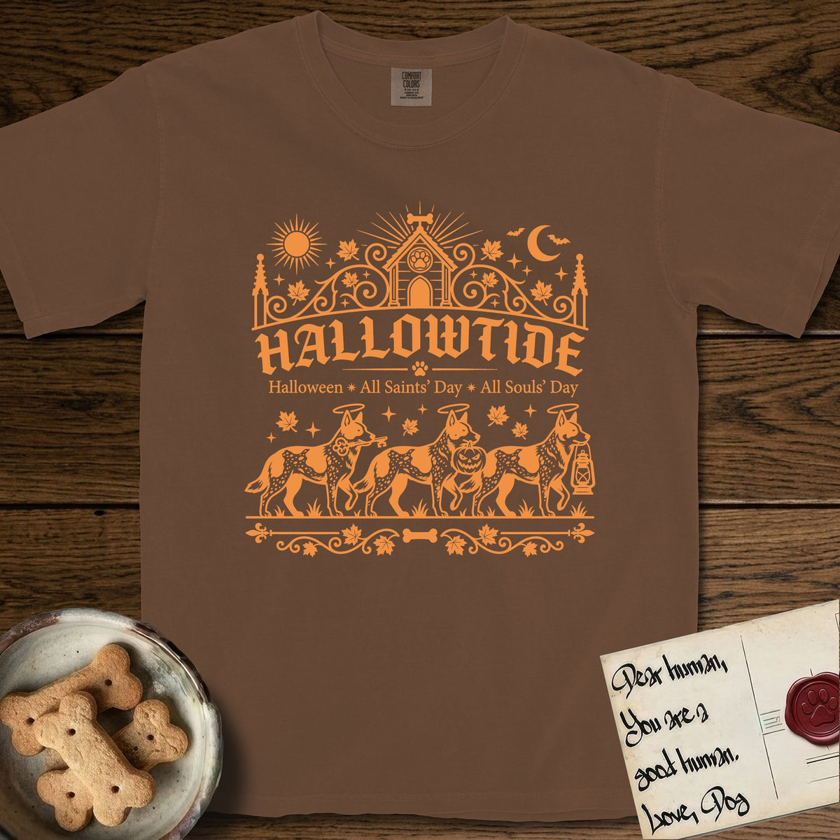 Hallowtide Australian Cattle Dog T-Shirt flat lay in Espresso, featuring Orange one-color gothic illustration of three haloed speckled Australian Cattle Dogs walking in procession carrying a skeleton key, a scary jack-o'-lantern, and an iron lantern, under the blackletter headline HALLOWTIDE.