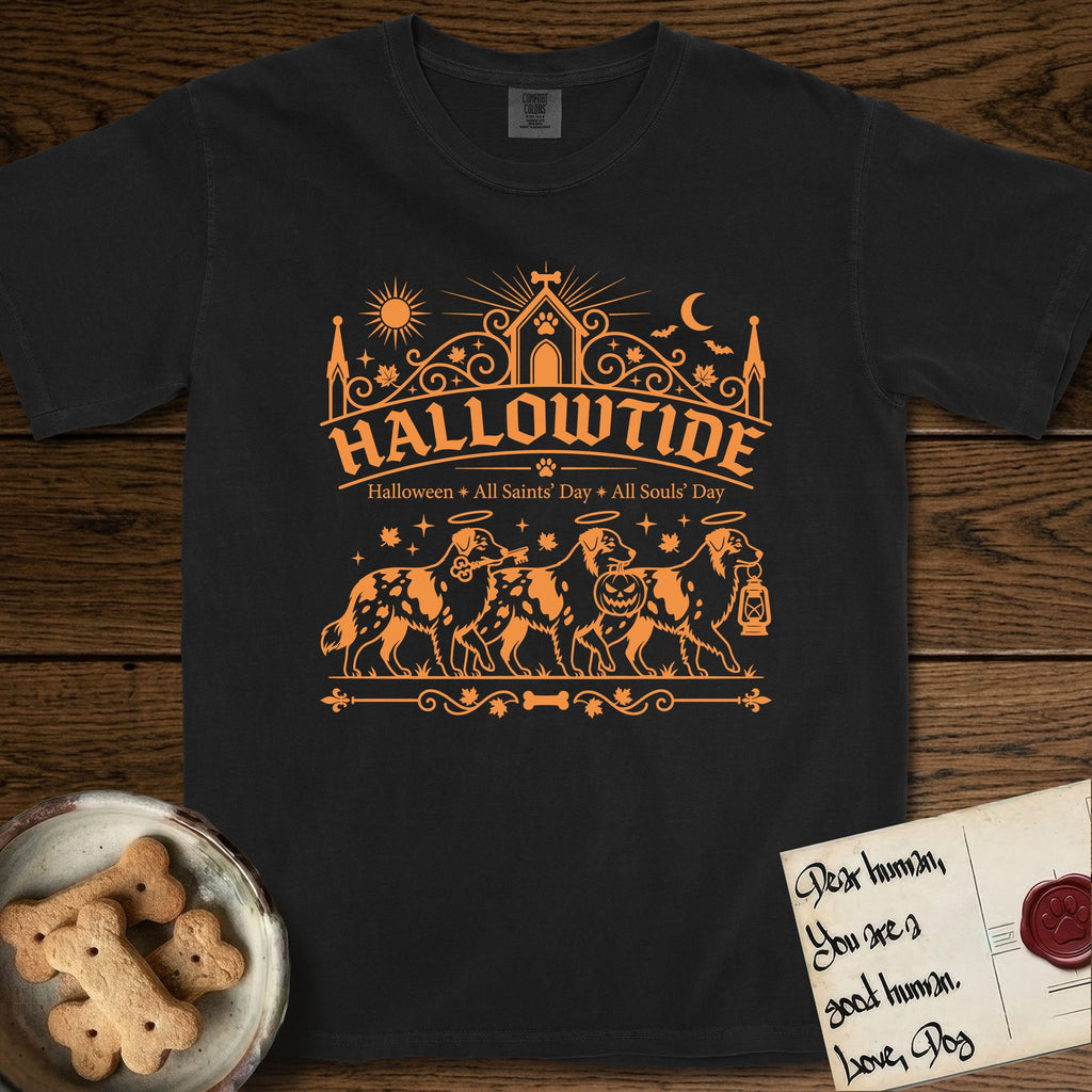 Hallowtide Australian Shepherd T-Shirt flat lay in Black, featuring Orange one-color gothic illustration of three haloed merle Australian Shepherds walking in procession carrying a skeleton key, a scary jack-o'-lantern, and an iron lantern, under the blackletter headline HALLOWTIDE.