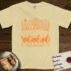 Hallowtide Bernese Mountain Dog T-Shirt flat lay in Butter, featuring Orange one-color gothic illustration of three haloed Bernese Mountain Dogs walking in procession carrying a skeleton key, a scary jack-o'-lantern, and an iron lantern, under the blackletter headline HALLOWTIDE.