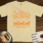 Hallowtide Black Lab T-Shirt flat lay in Butter, featuring Orange one-color gothic illustration of three haloed Black Labs walking in procession carrying a skeleton key, a scary jack-o'-lantern, and an iron lantern, under the blackletter headline HALLOWTIDE.