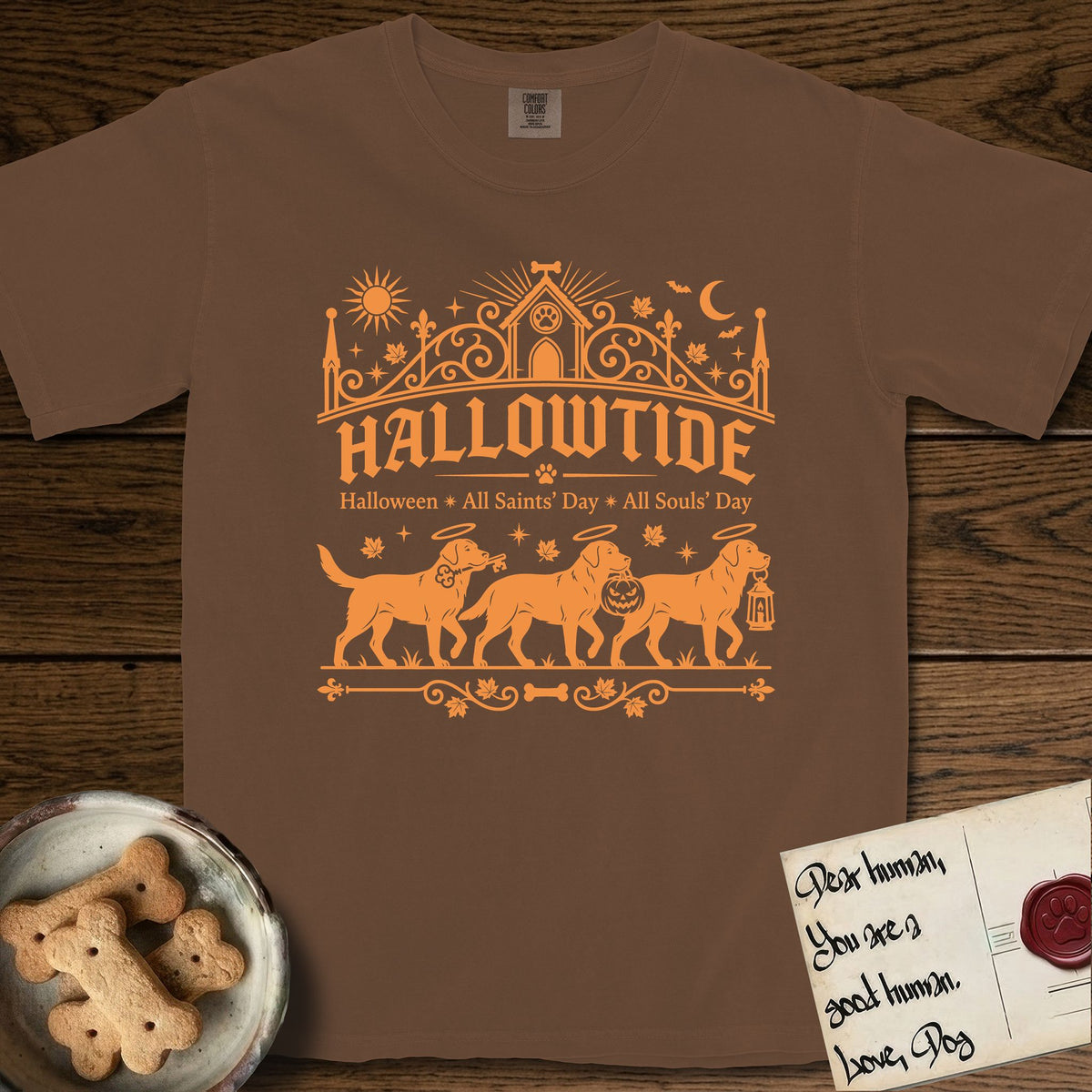Hallowtide Black Lab T-Shirt flat lay in Espresso, featuring Orange one-color gothic illustration of three haloed Black Labs walking in procession carrying a skeleton key, a scary jack-o'-lantern, and an iron lantern, under the blackletter headline HALLOWTIDE.