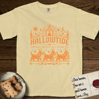 Hallowtide Cairn Terrier T-Shirt flat lay in Butter, featuring Orange one-color gothic illustration of three haloed shaggy Cairn Terriers walking in procession carrying a skeleton key, a scary jack-o'-lantern, and an iron lantern, under the blackletter headline HALLOWTIDE.