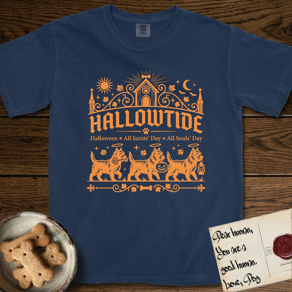 Hallowtide Cairn Terrier T-Shirt flat lay in True Navy, featuring Orange one-color gothic illustration of three haloed shaggy Cairn Terriers walking in procession carrying a skeleton key, a scary jack-o'-lantern, and an iron lantern, under the blackletter headline HALLOWTIDE.