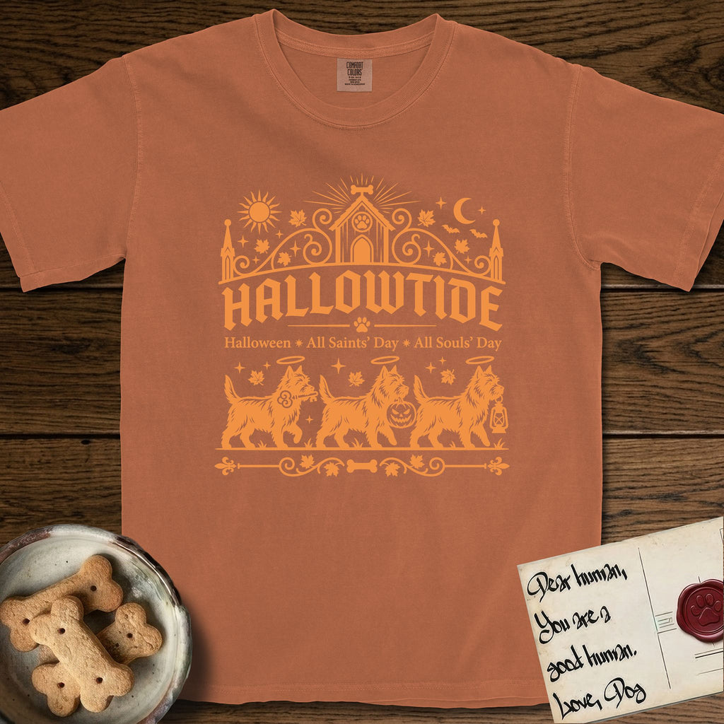 Hallowtide Cairn Terrier T-Shirt flat lay in Yam, featuring Orange one-color gothic illustration of three haloed shaggy Cairn Terriers walking in procession carrying a skeleton key, a scary jack-o'-lantern, and an iron lantern, under the blackletter headline HALLOWTIDE.