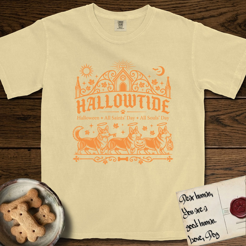 Hallowtide Corgi T-Shirt flat lay in Butter, featuring Orange one-color gothic illustration of three haloed Corgis walking in procession carrying a skeleton key, a scary jack-o'-lantern, and an iron lantern, under the blackletter headline HALLOWTIDE.