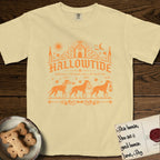 Hallowtide Doberman T-Shirt flat lay in Butter, featuring Orange one-color gothic illustration of three haloed Dobermans walking in procession carrying a skeleton key, a scary jack-o'-lantern, and an iron lantern, under the blackletter headline HALLOWTIDE.