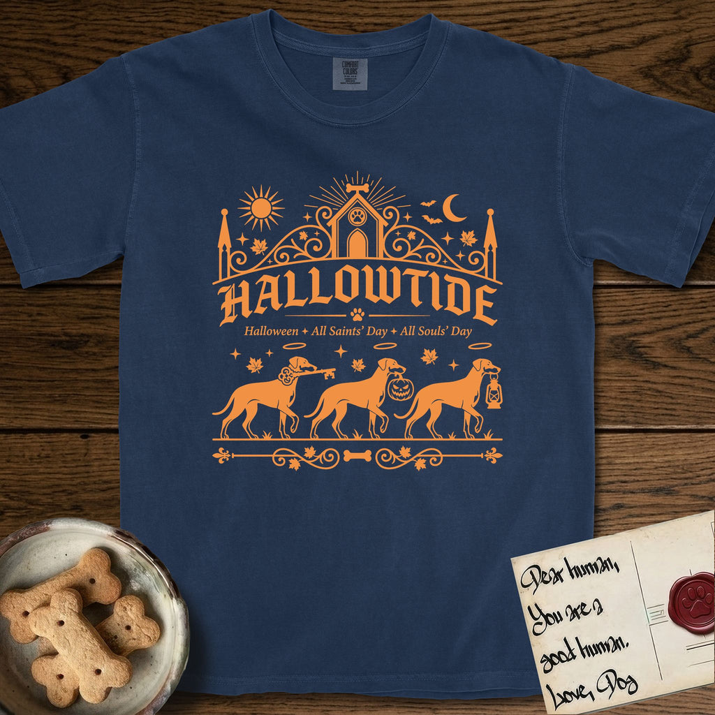 Hallowtide Doberman T-Shirt flat lay in True Navy, featuring Orange one-color gothic illustration of three haloed Dobermans walking in procession carrying a skeleton key, a scary jack-o'-lantern, and an iron lantern, under the blackletter headline HALLOWTIDE.