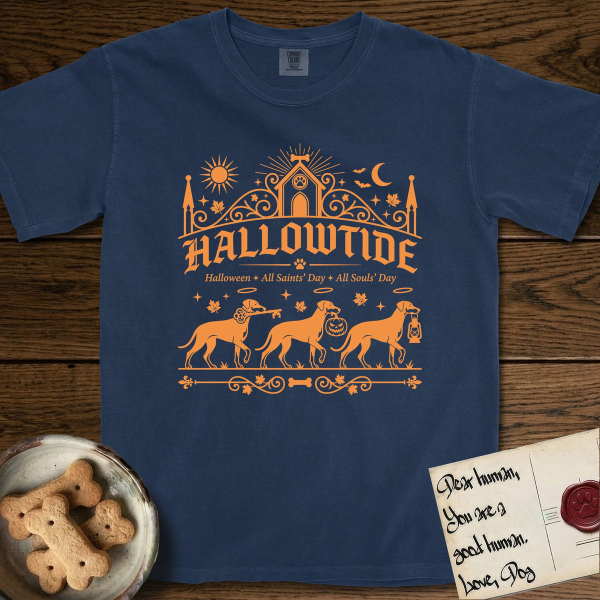 Hallowtide Doberman T-Shirt flat lay in True Navy, featuring Orange one-color gothic illustration of three haloed Dobermans walking in procession carrying a skeleton key, a scary jack-o'-lantern, and an iron lantern, under the blackletter headline HALLOWTIDE.
