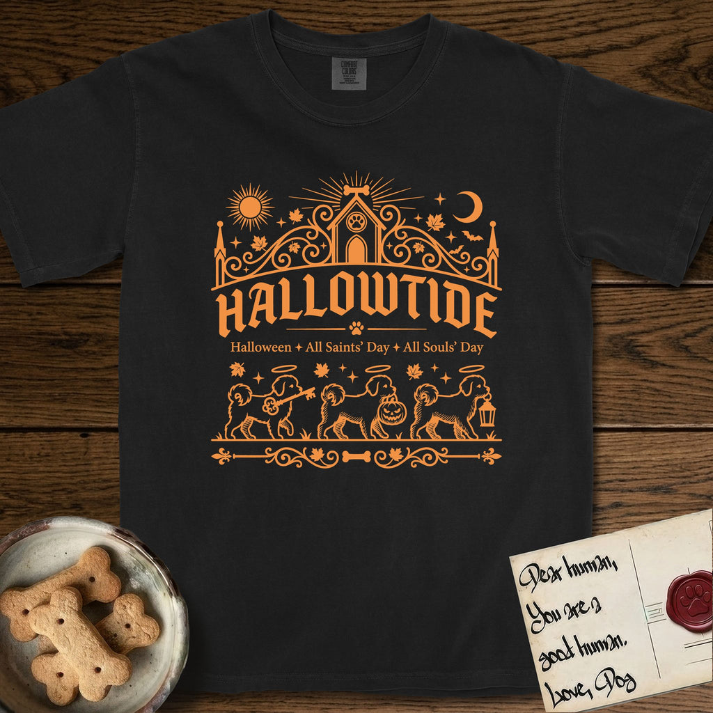 Hallowtide Maltese T-Shirt flat lay in Black, featuring Orange one-color gothic illustration of three haloed Maltese walking in procession carrying a skeleton key, a scary jack-o'-lantern, and an iron lantern, under the blackletter headline HALLOWTIDE.