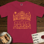 Hallowtide Maltese T-Shirt flat lay in Chili, featuring Orange one-color gothic illustration of three haloed Maltese walking in procession carrying a skeleton key, a scary jack-o'-lantern, and an iron lantern, under the blackletter headline HALLOWTIDE.