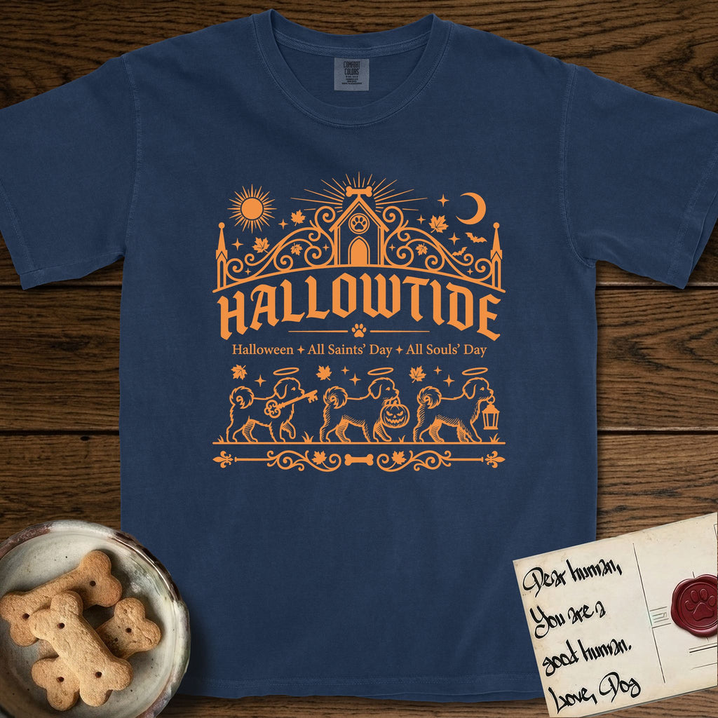 Hallowtide Maltese T-Shirt flat lay in True Navy, featuring Orange one-color gothic illustration of three haloed Maltese walking in procession carrying a skeleton key, a scary jack-o'-lantern, and an iron lantern, under the blackletter headline HALLOWTIDE.