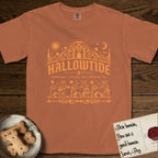 Hallowtide Maltese T-Shirt flat lay in Yam, featuring Orange one-color gothic illustration of three haloed Maltese walking in procession carrying a skeleton key, a scary jack-o'-lantern, and an iron lantern, under the blackletter headline HALLOWTIDE.