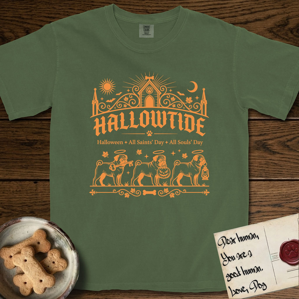 Hallowtide Pug T-Shirt flat lay in Moss, featuring Orange one-color gothic illustration of three haloed curly-tailed Pugs walking in procession carrying a skeleton key, a scary jack-o'-lantern, and an iron lantern, under the blackletter headline HALLOWTIDE.