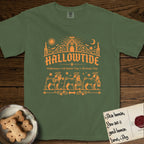 Hallowtide Pug T-Shirt flat lay in Moss, featuring Orange one-color gothic illustration of three haloed curly-tailed Pugs walking in procession carrying a skeleton key, a scary jack-o'-lantern, and an iron lantern, under the blackletter headline HALLOWTIDE.