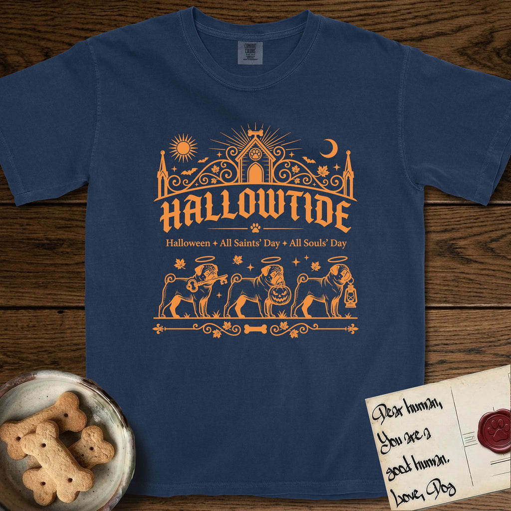 Hallowtide Pug T-Shirt flat lay in True Navy, featuring Orange one-color gothic illustration of three haloed curly-tailed Pugs walking in procession carrying a skeleton key, a scary jack-o'-lantern, and an iron lantern, under the blackletter headline HALLOWTIDE.