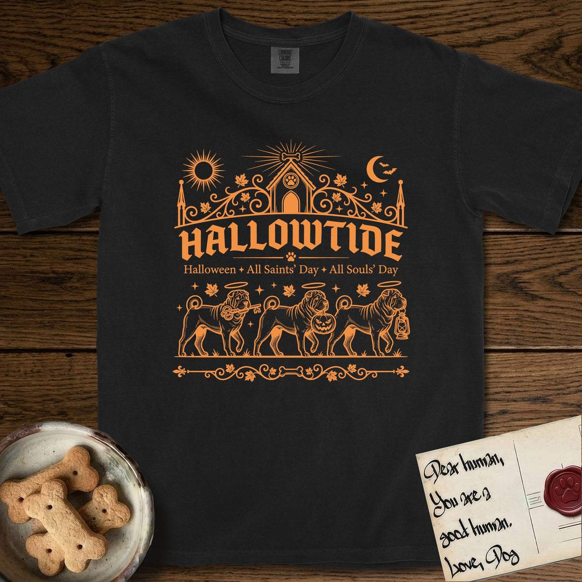 Hallowtide Shar-Pei T-Shirt flat lay in Black, featuring Orange one-color gothic illustration of three haloed wrinkled Shar-Peis walking in procession carrying a skeleton key, a scary jack-o'-lantern, and an iron lantern, under the blackletter headline HALLOWTIDE.