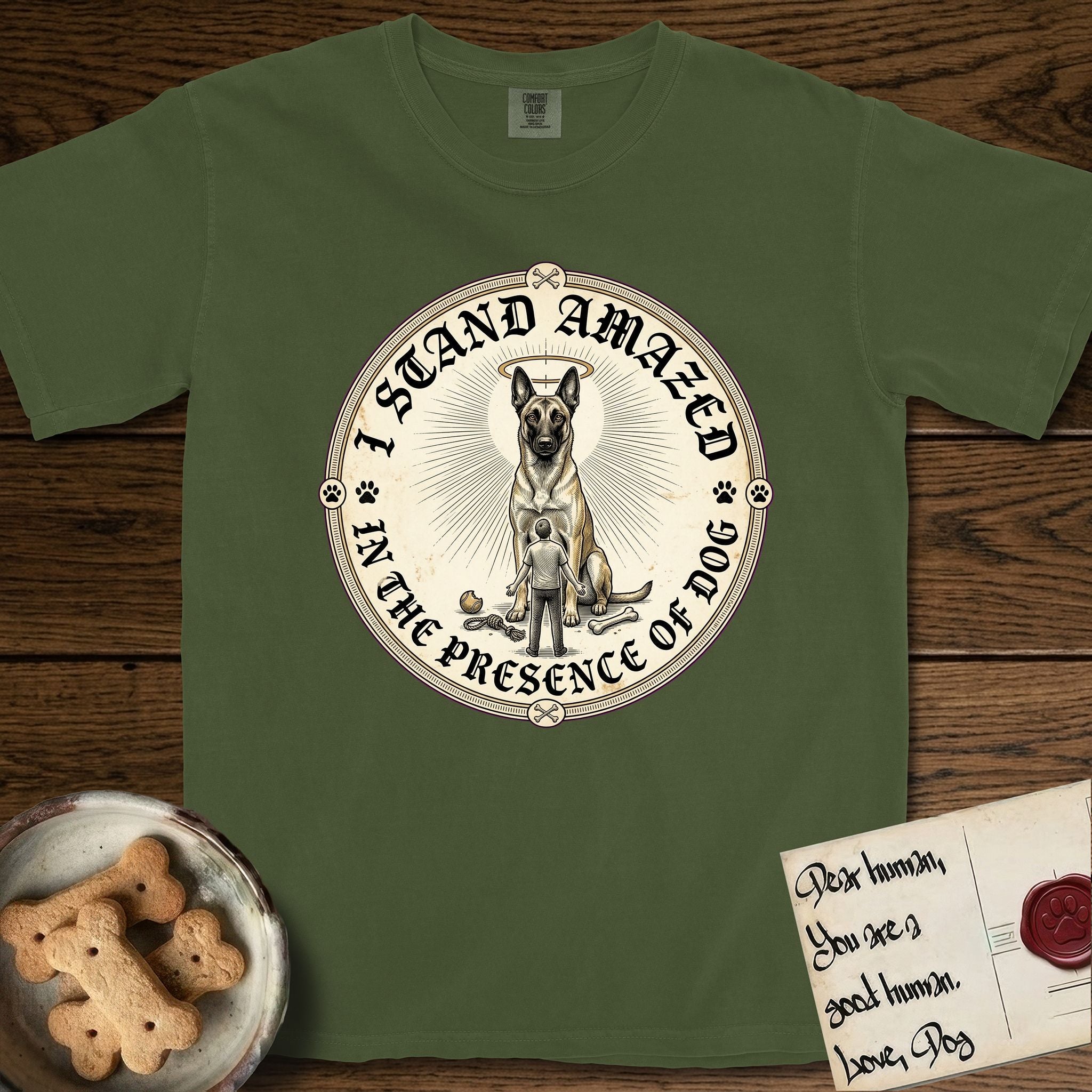 I Stand Amazed in the Presence Belgian Malinois T-Shirt flat lay in Hemp, featuring a vintage engraving medallion of a haloed Belgian Malinois with a small devoted human gazing up from below.