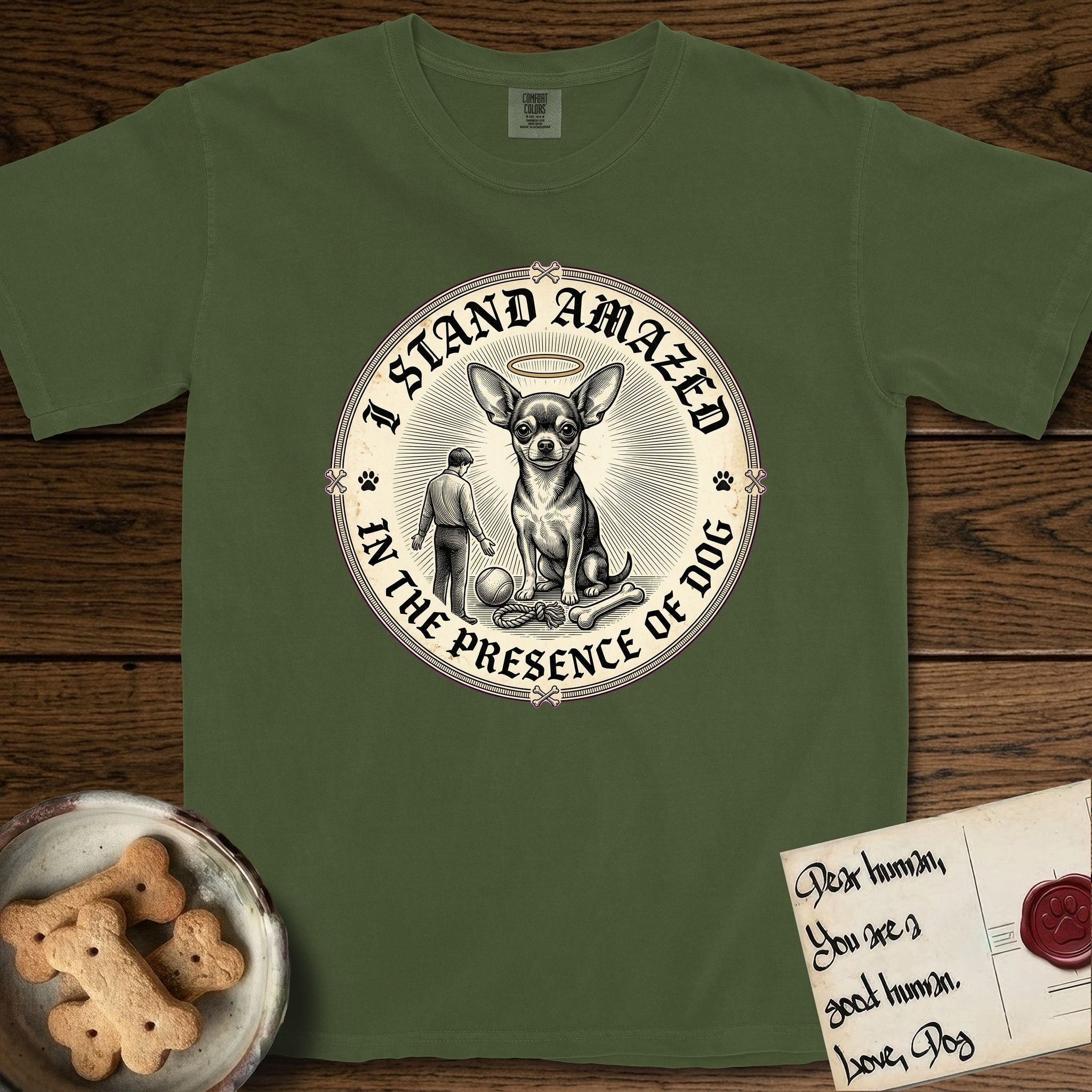 I Stand Amazed in the Presence Chihuahua T-Shirt flat lay in Hemp, featuring a vintage engraving medallion of a haloed Chihuahua with a small devoted human gazing up from below.