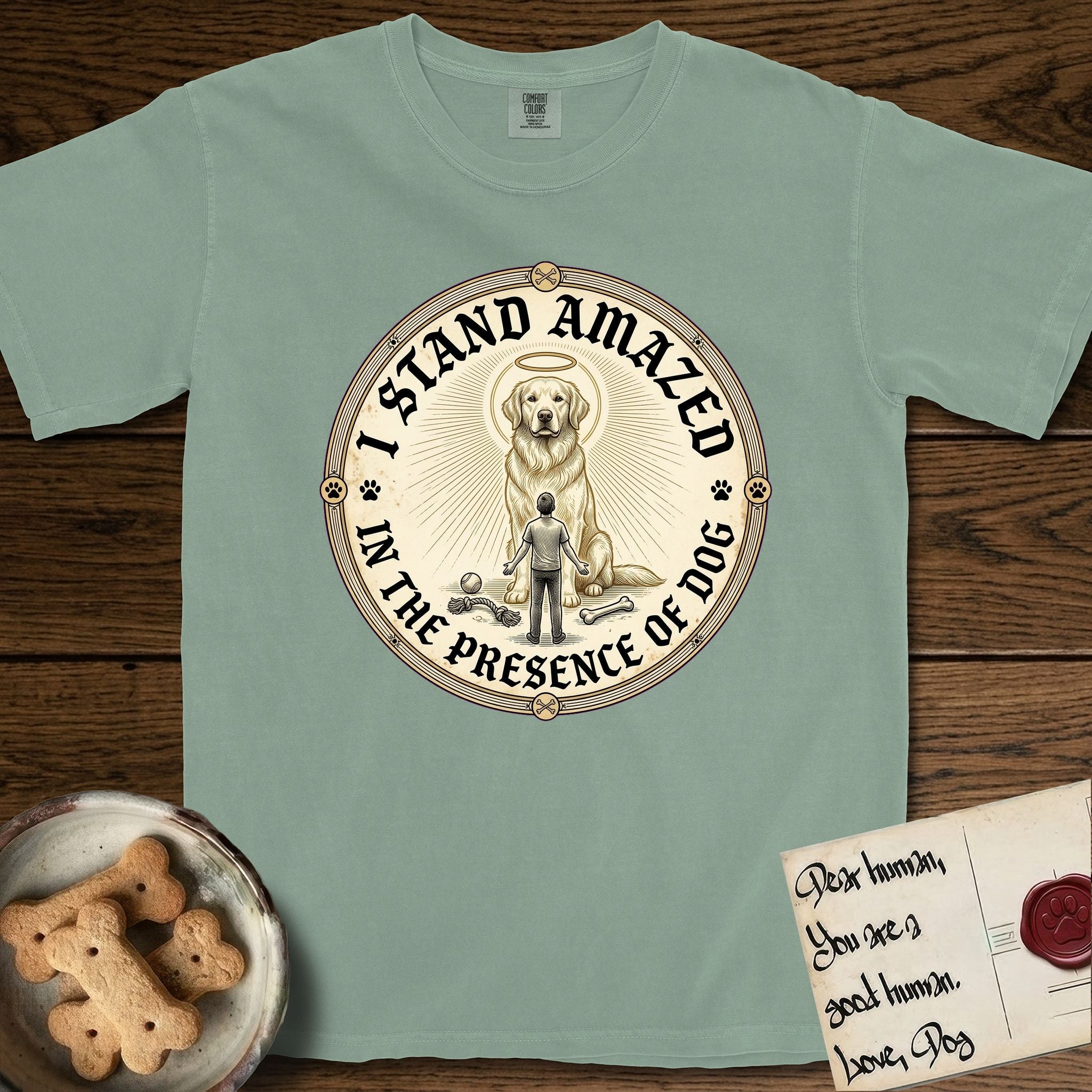 I Stand Amazed in the Presence Golden Retriever T-Shirt flat lay in Bay, featuring a vintage engraving medallion of a haloed Golden Retriever with a small devoted human gazing up from below.