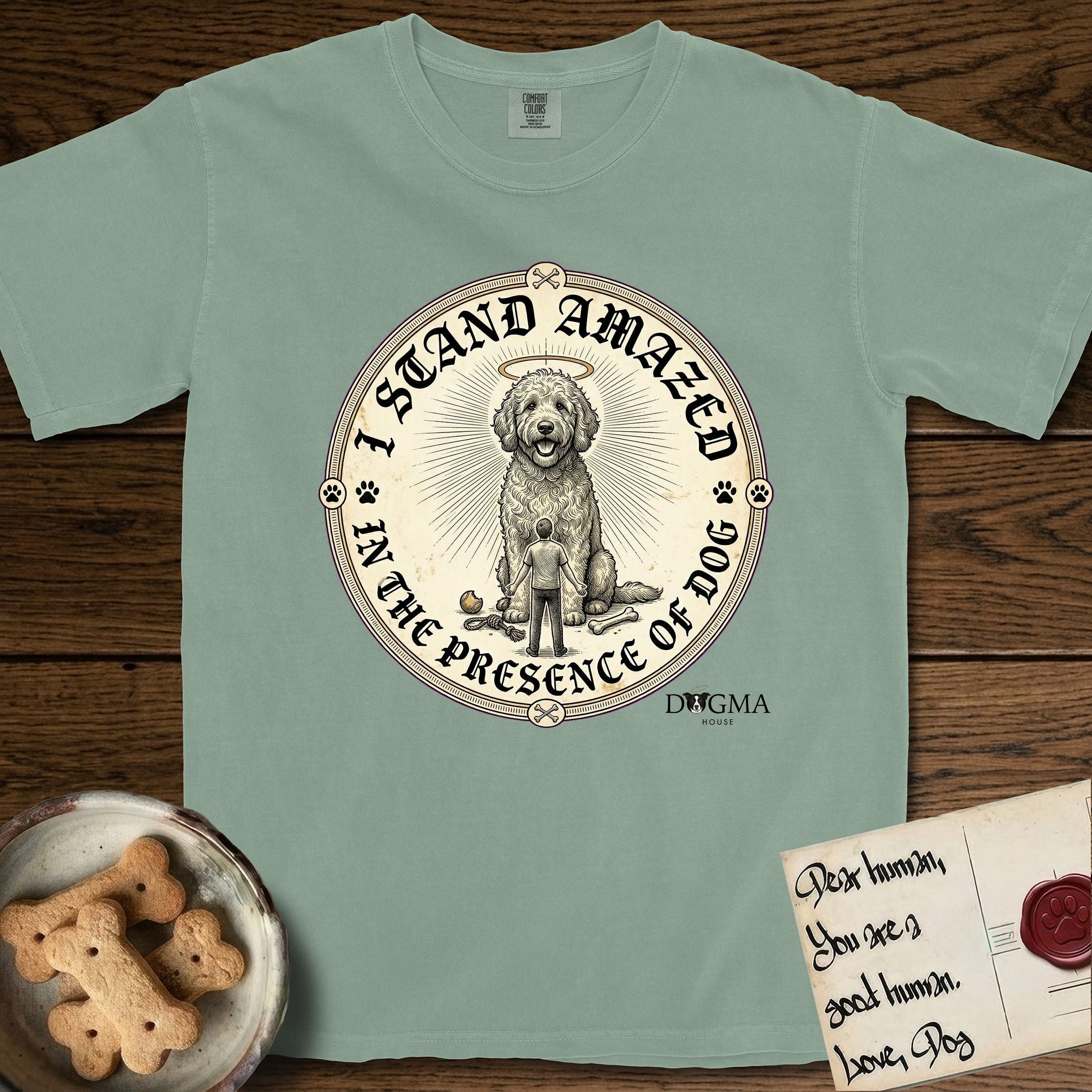 I Stand Amazed in the Presence Goldendoodle T-Shirt flat lay in Bay, featuring a vintage engraving medallion of a haloed Goldendoodle with a small devoted human gazing up from below.